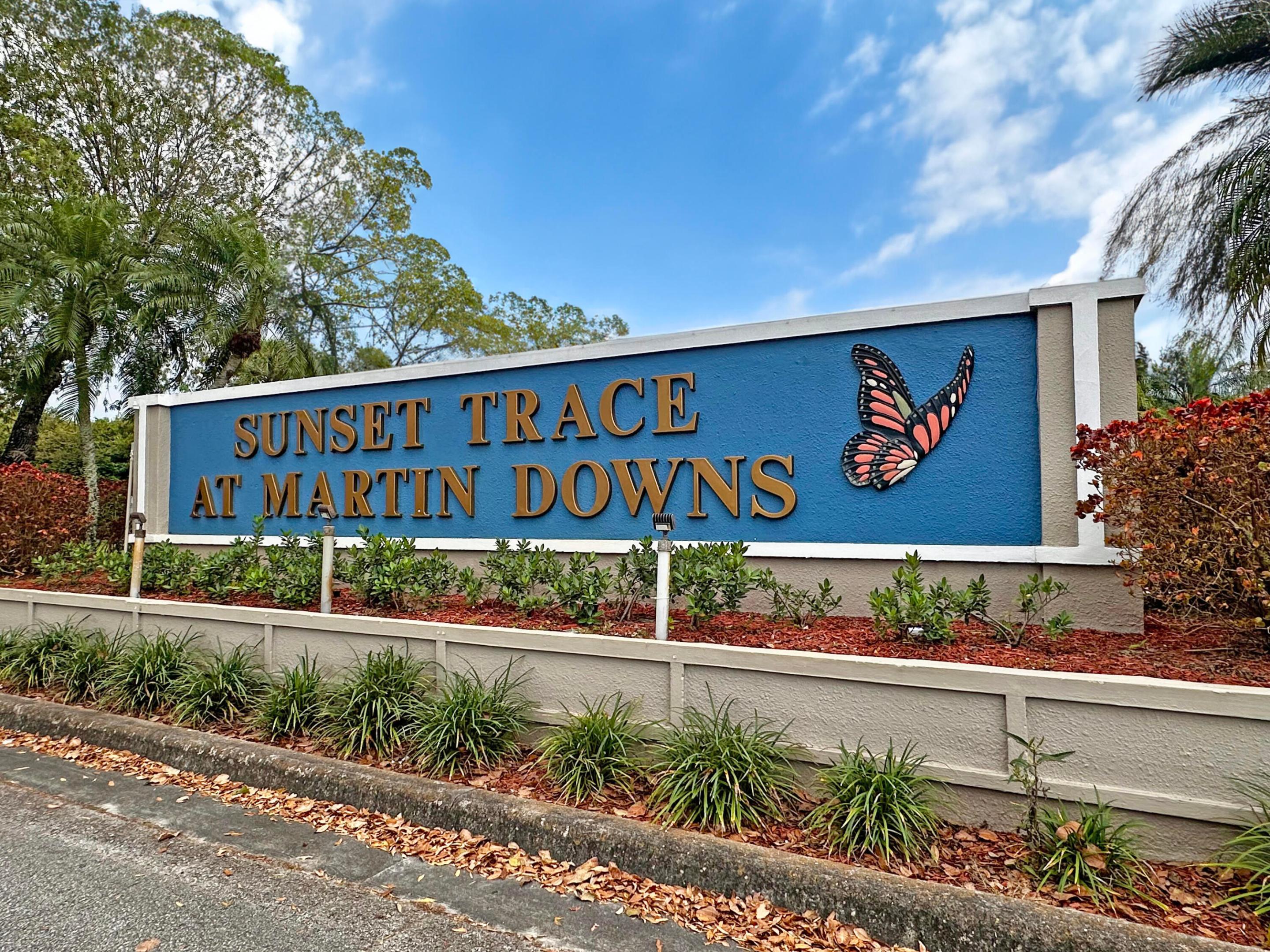 Community entrance monument sign featuring stucco siding, integrated landscape lighting, and decorative butterfly accent