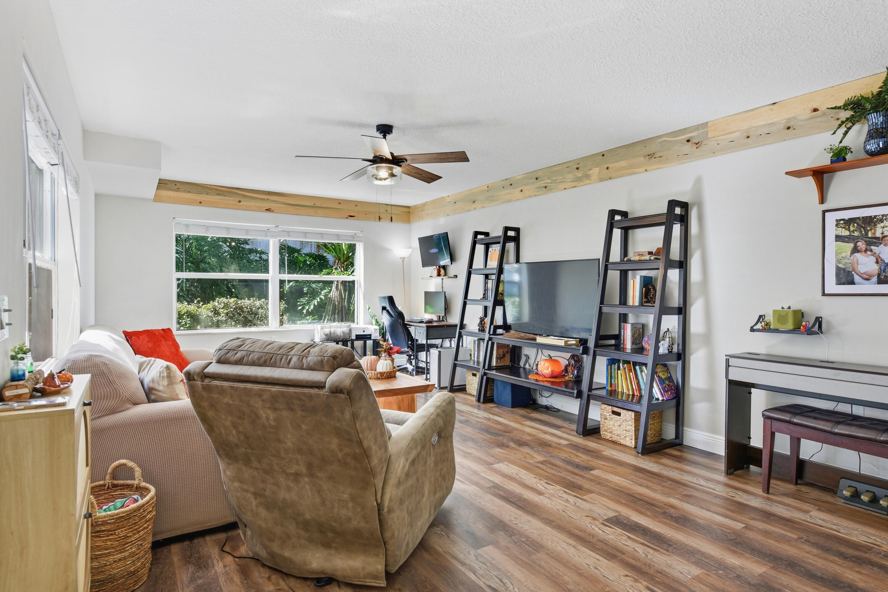 Living area featuring wood-finish flooring, exposed natural wood ceiling beams, and a central ceiling fan