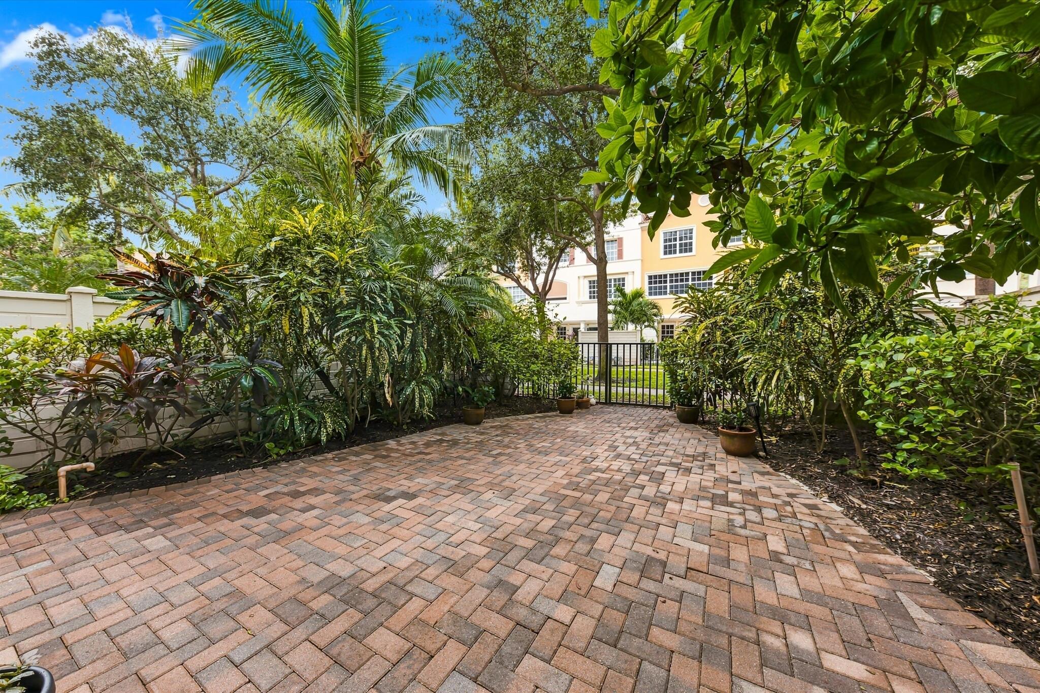 Private patio featuring herringbone-patterned brick pavers, enclosed by high perimeter fencing and lush mature landscaping