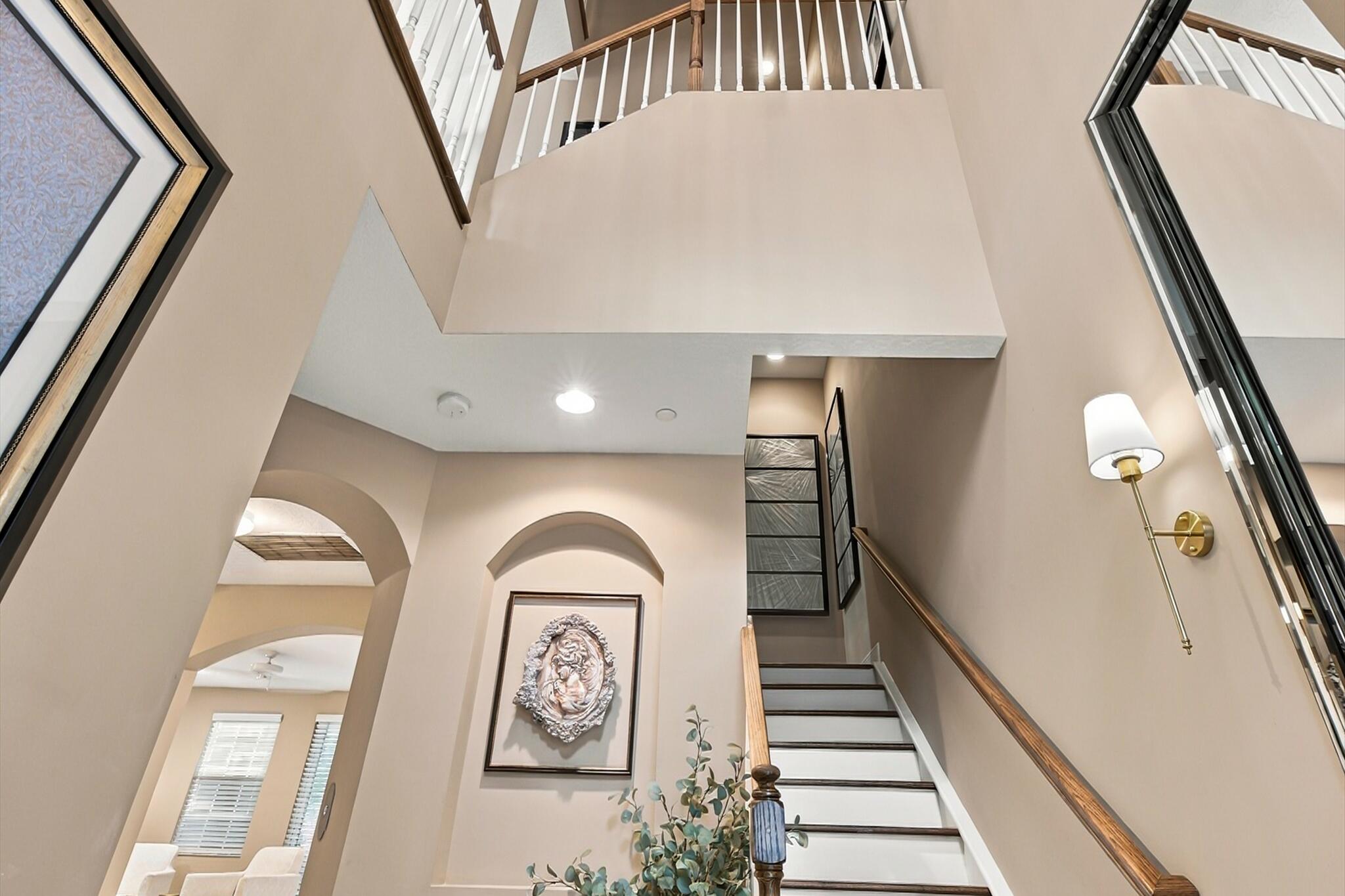 Double-height entry featuring an arched recessed wall niche, staircase with a wood handrail and white balusters, and wall-mounted brass lighting