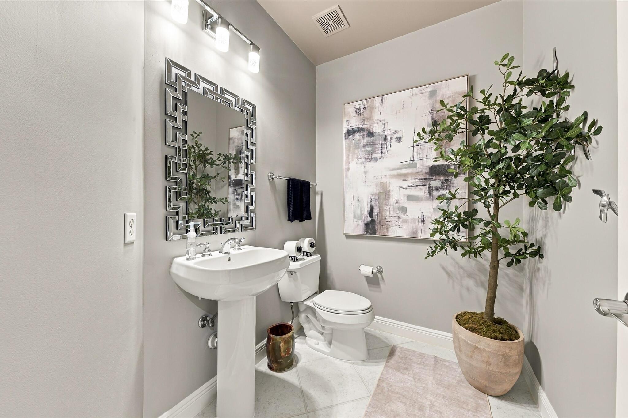 Porcelain pedestal sink with polished chrome hardware, geometric framed wall mirror, three-bulb vanity light fixture, and tile flooring