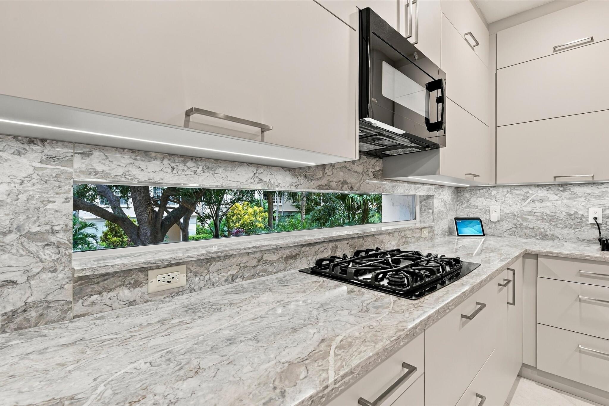 Kitchen featuring high-gloss cabinetry, stone countertops and backsplash, integrated horizontal window, and black gas cooktop with matching built-in microwave