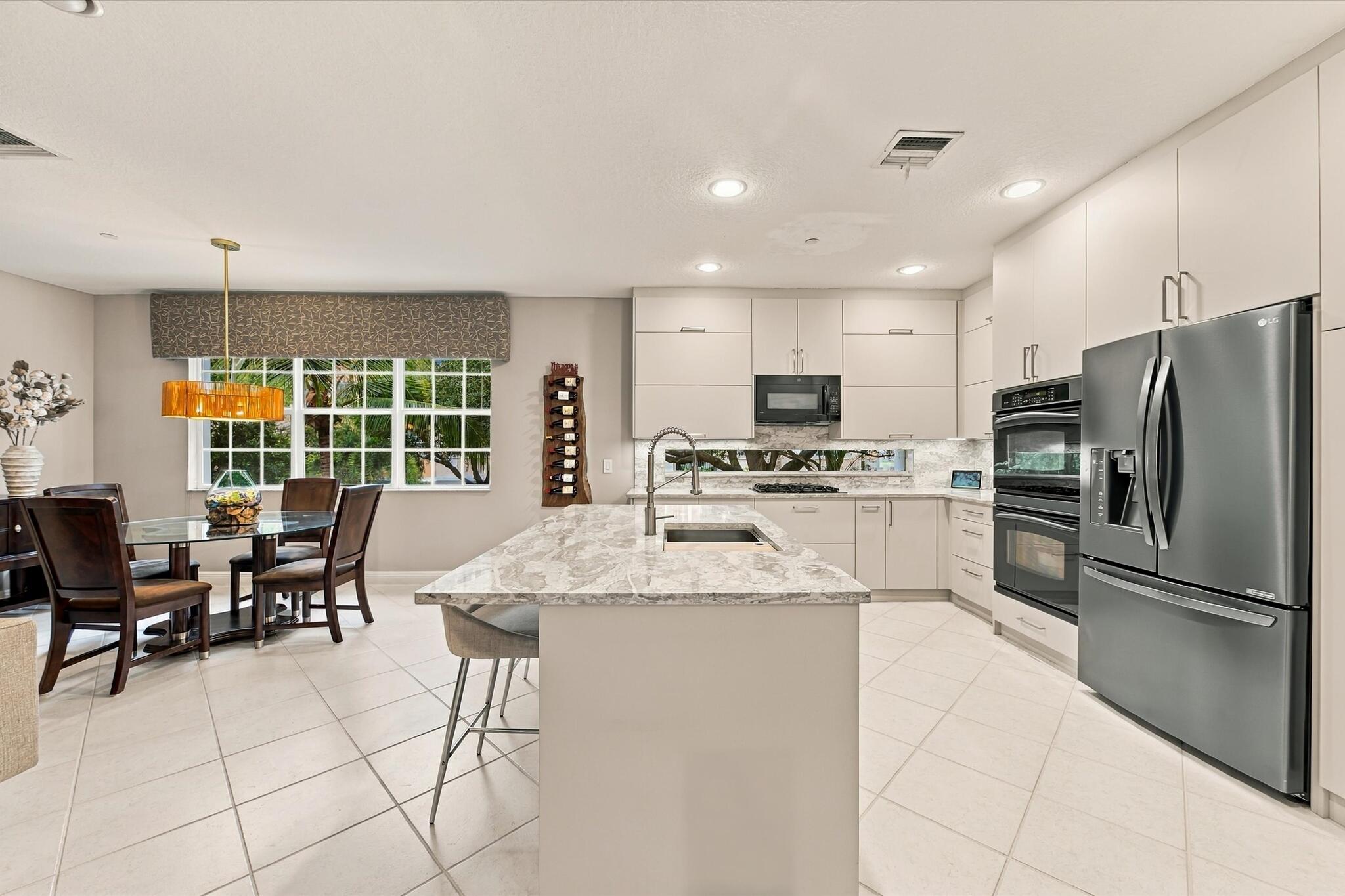 Kitchen featuring flat-panel cabinetry, a stone-surface island with an integrated sink, built-in stainless steel double wall ovens, a recessed microwave, and tile flooring