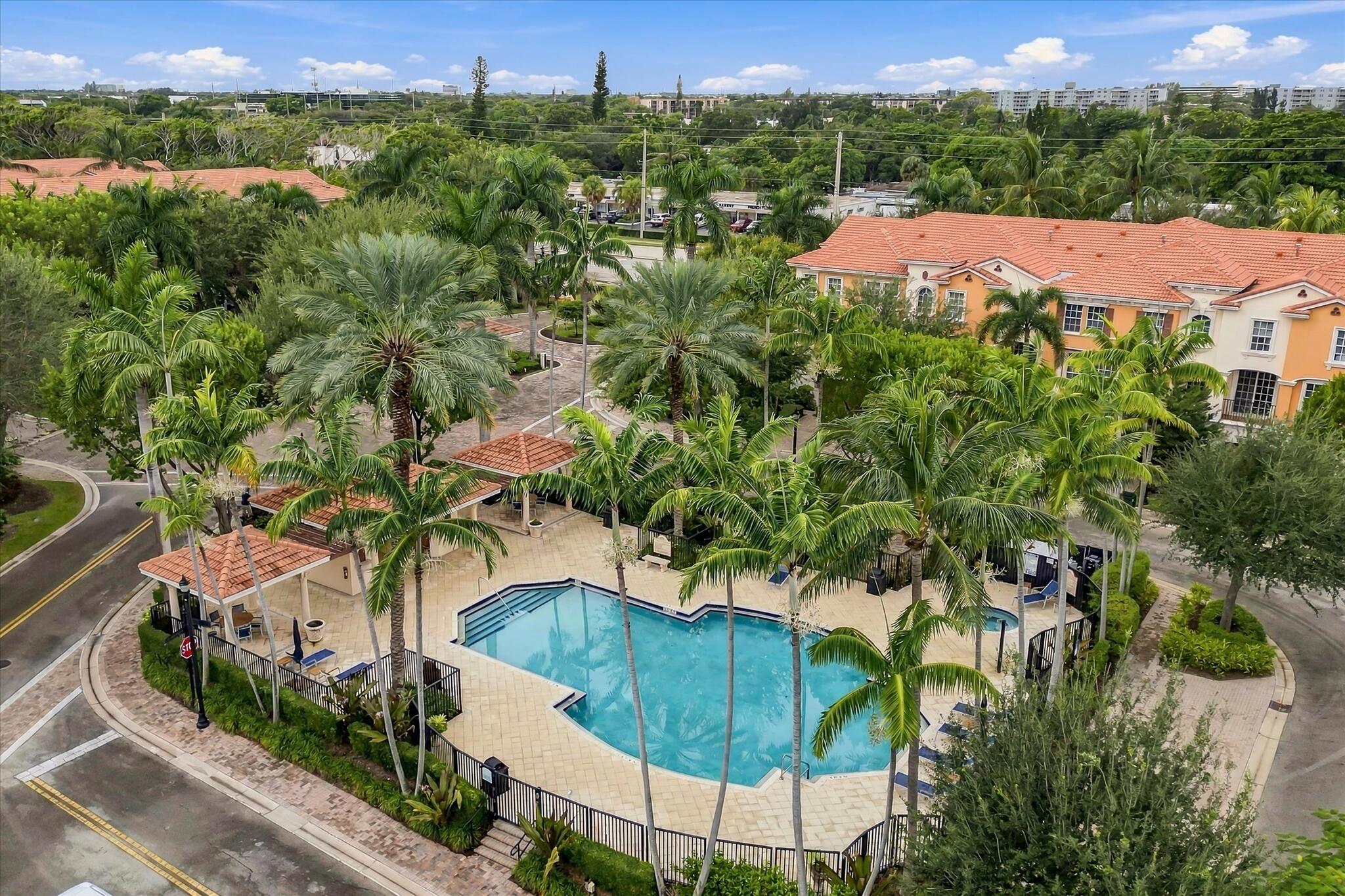 Community swimming pool with stone decking, integrated spa, and covered pergola structures, surrounded by manicured landscaping and mature palm trees