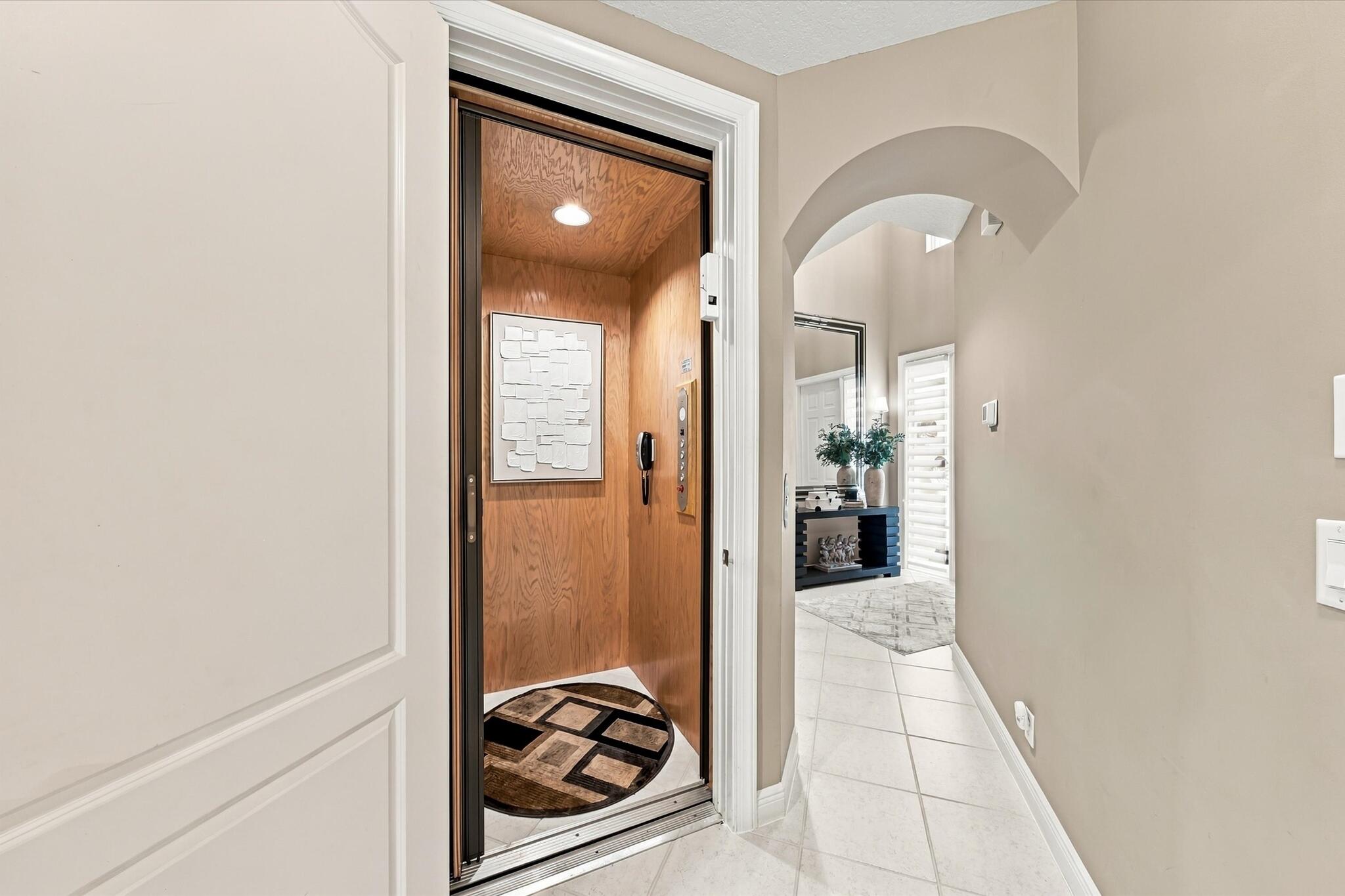 In-home elevator with wood-paneled interior and recessed lighting, featuring an arched entryway and light-toned tile flooring