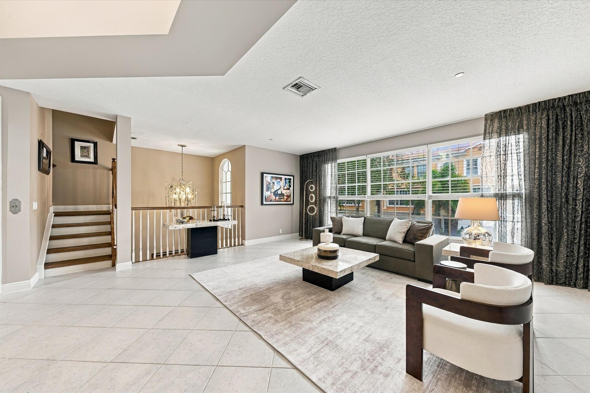 Open-concept interior featuring large-format tile flooring, multi-pane windows, arched window detail, and a staircase with wood treads and a baluster railing