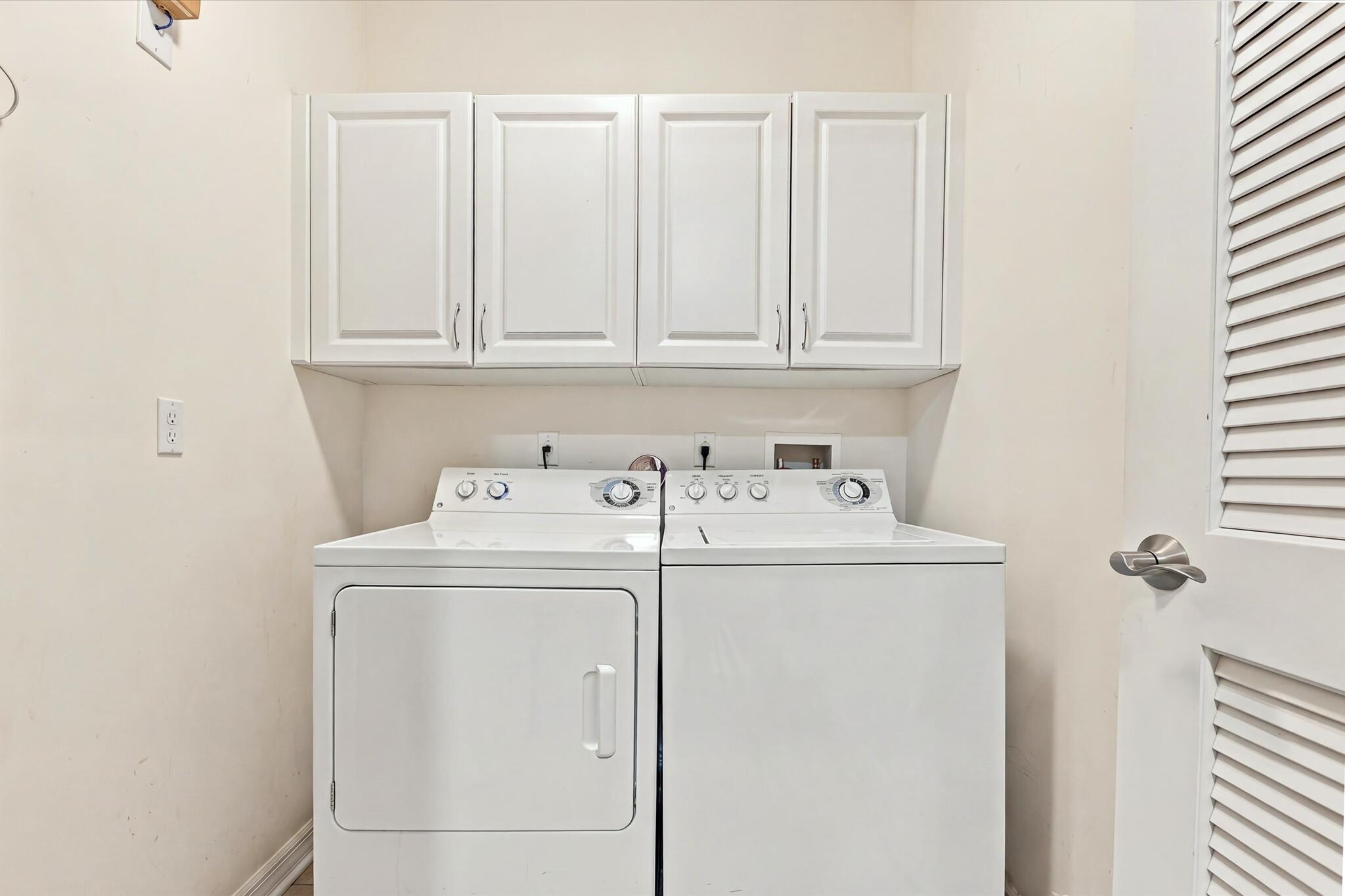 Laundry space featuring white upper cabinetry and a louvered door