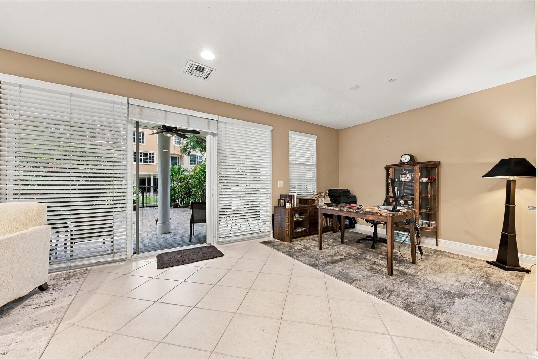 Neutral-toned interior featuring large-format tile flooring, recessed lighting, and expansive sliding glass doors with horizontal blinds, providing access to an exterior paved patio