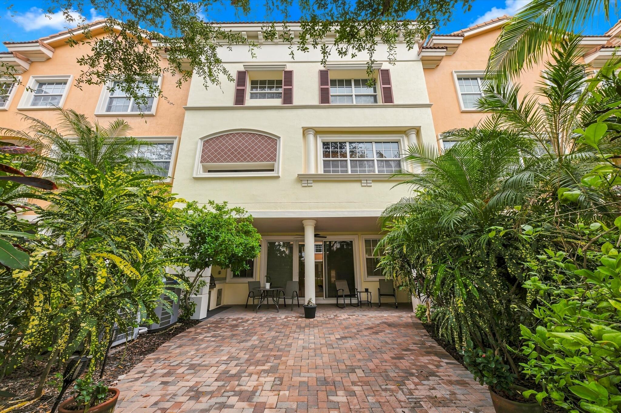 Stucco exterior featuring multi-story architectural detailing, brick-paver patio, decorative window shutters, and columns supporting a covered terrace