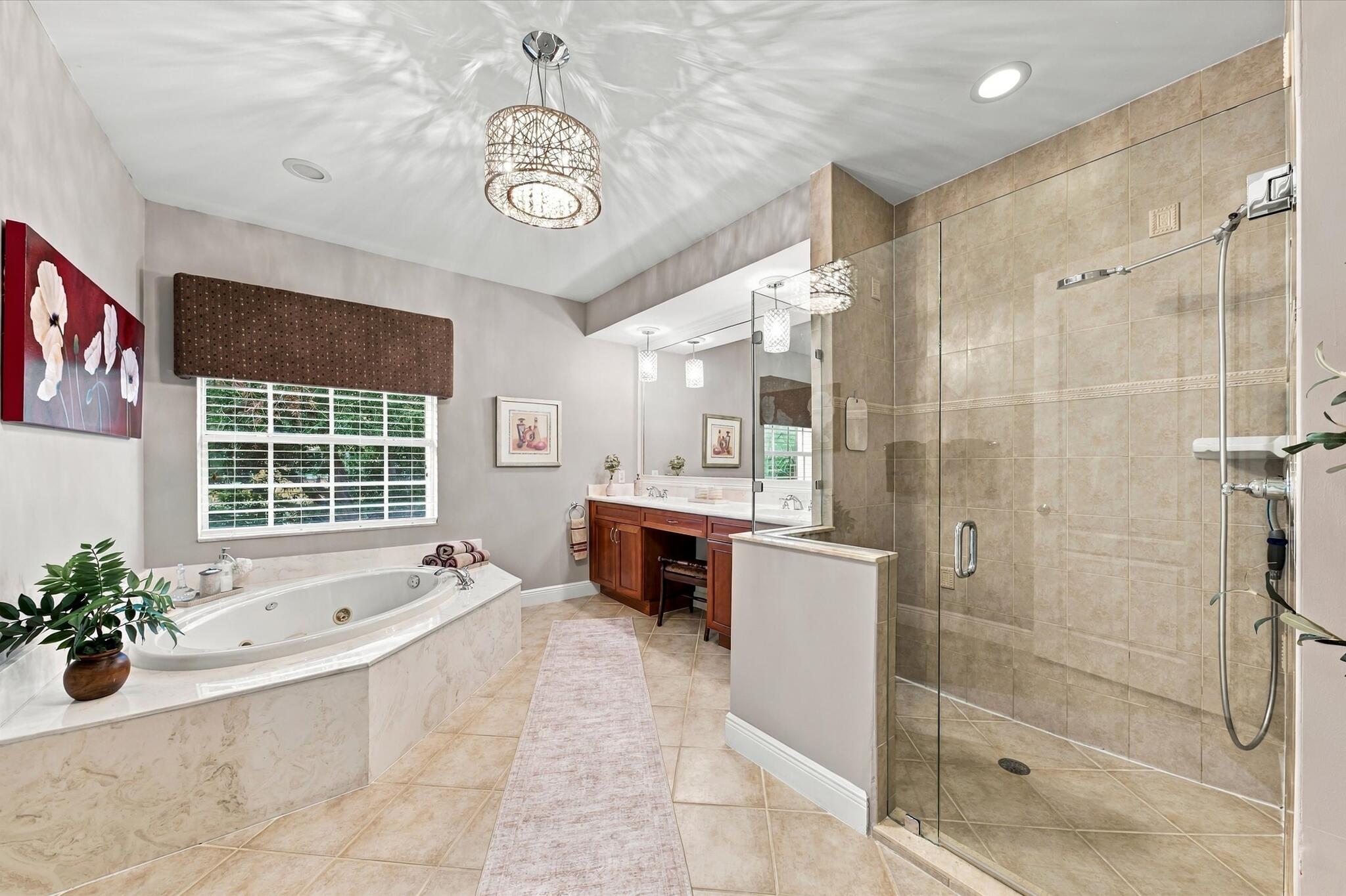 Jetted soaking tub with tile surround, walk-in glass-enclosed shower, dual-sink vanity with built-in cabinetry, crystal-accented light fixture, and tile flooring