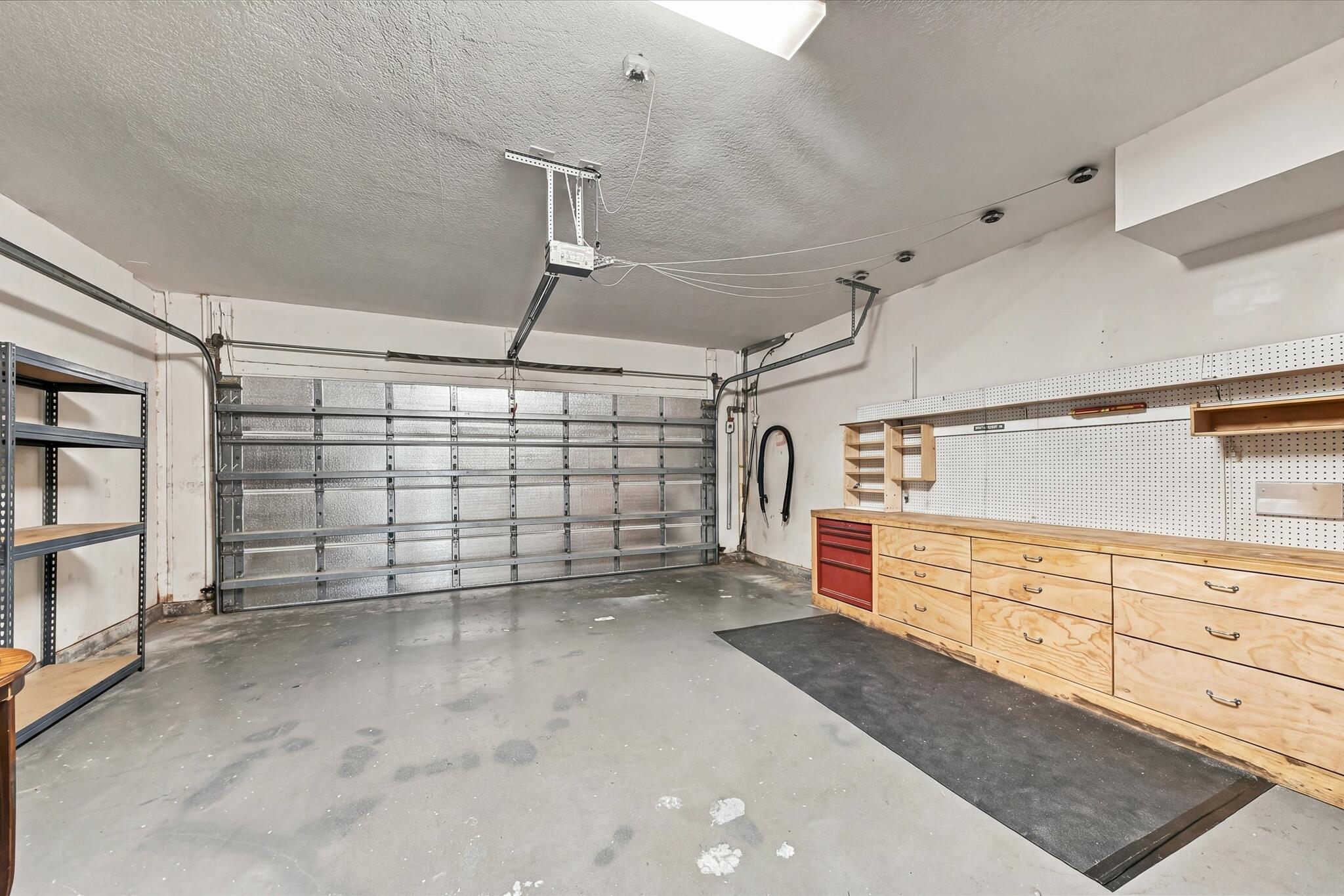 Attached two-car garage featuring a metal overhead door, custom built-in wood cabinetry, integrated pegboard wall organization, and finished concrete flooring