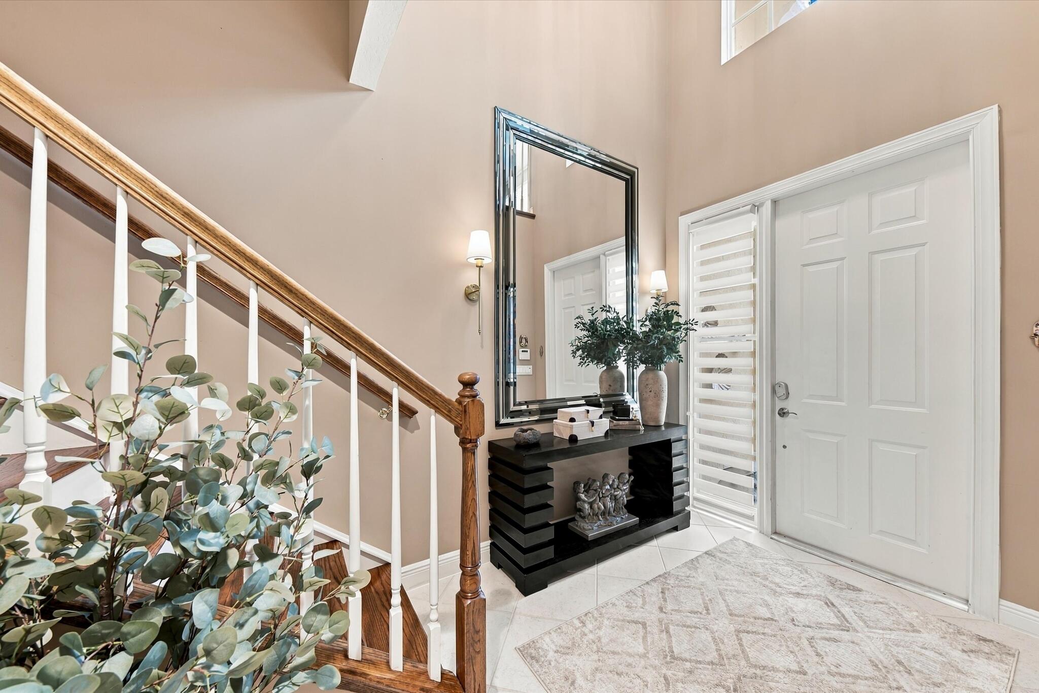 Foyer featuring a double-height ceiling, staircase with wood handrails and white balusters, multi-panel entry door with sidelight, tile flooring, and wall-mounted light fixtures