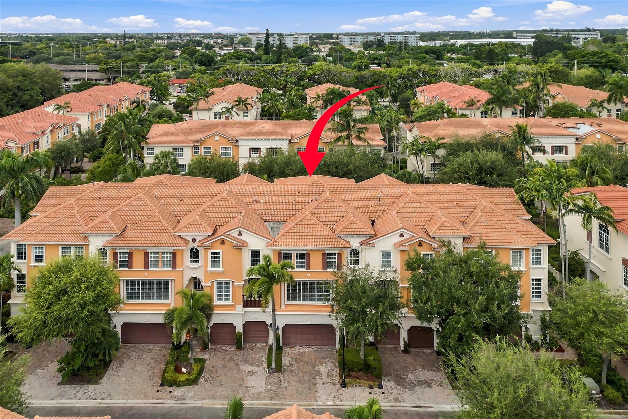 Multi-story townhome exterior featuring terracotta-style roof tiles, stucco facade, multi-car garage, and mature landscaping