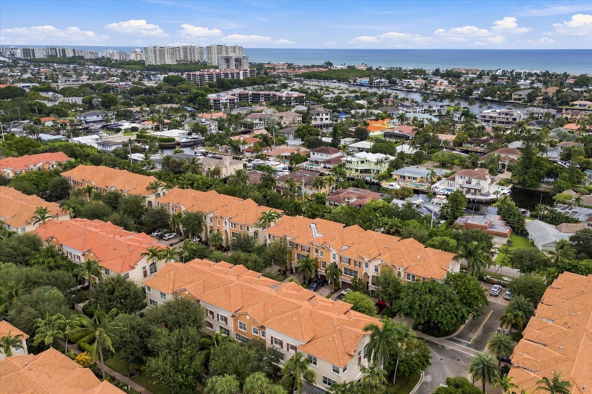 Aerial view featuring Mediterranean-style architecture with clay tile roofs, mature palm trees, and proximity to the coastline