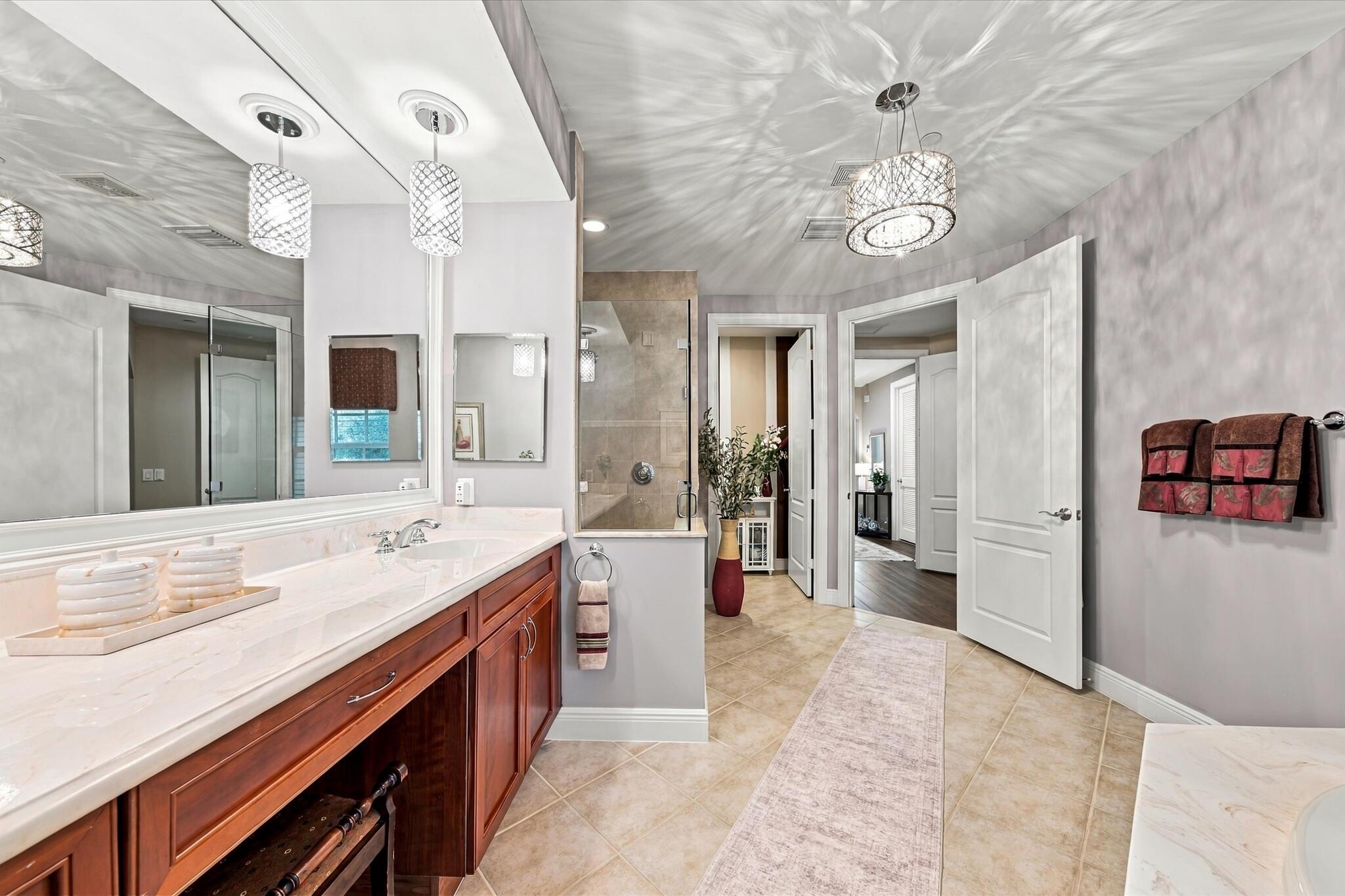 Bathroom vanity featuring a light-toned stone countertop, dual undermount sinks, wood-finish cabinetry, and decorative glass pendant lighting