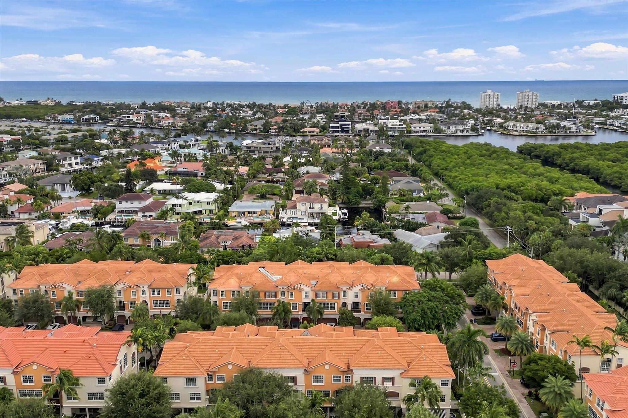 Aerial perspective of a multi-unit complex featuring terra-cotta tile roofs, stucco exterior finish, mature palm trees, and proximity to coastal waterways