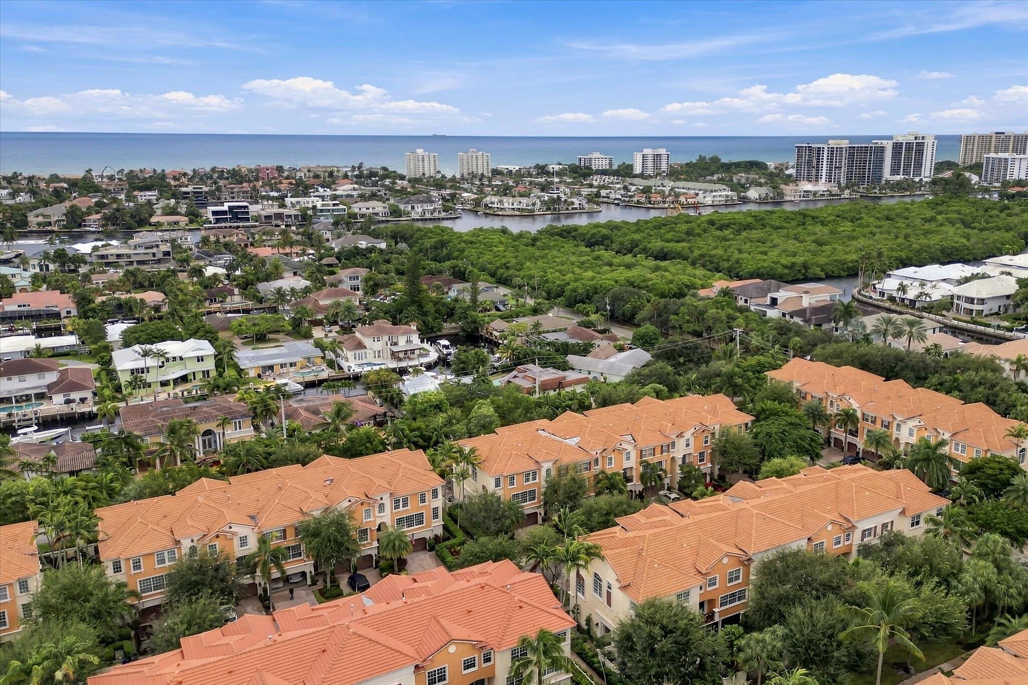 Aerial perspective of a multi-unit residential community featuring terra-cotta tile roofs, dense tropical landscaping, and proximity to coastal waterways