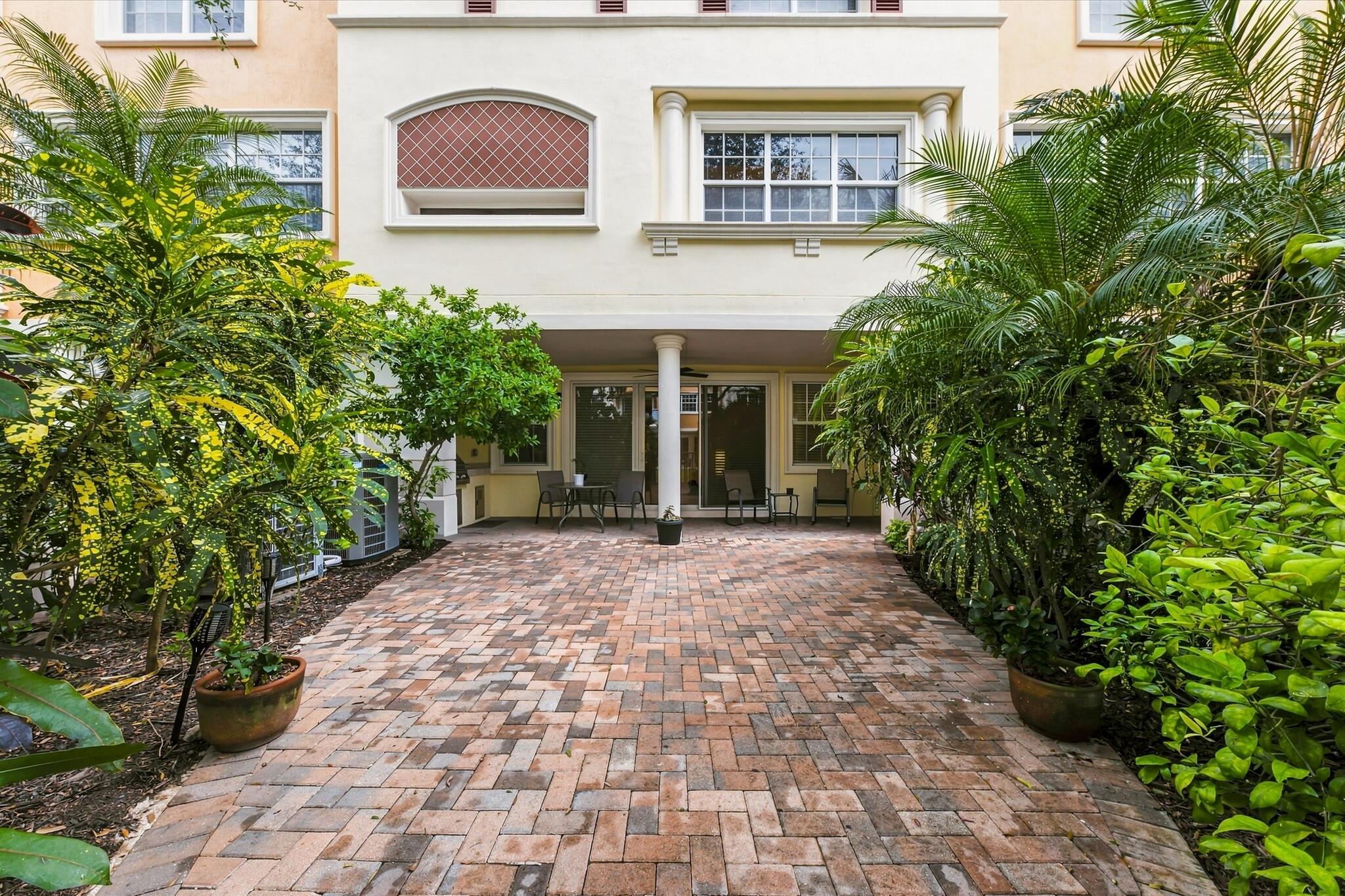 Brick-paved patio featuring a covered loggia, classical columns, and multi-story stucco facade with decorative stonework detailing