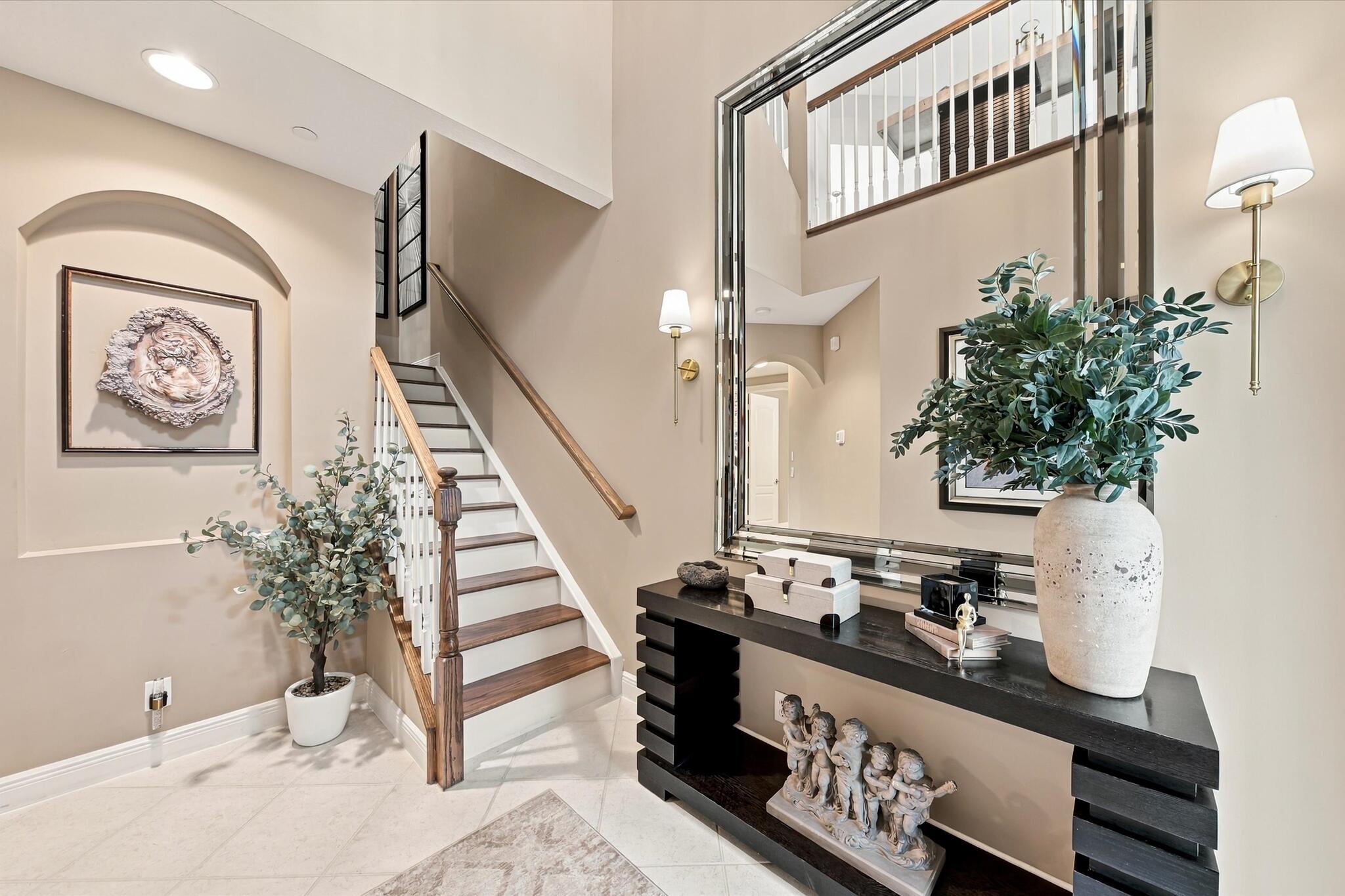 Two-story foyer featuring tile flooring, an arched recessed wall niche, a staircase with wood-finish treads and a white balustrade, and wall-mounted light fixtures
