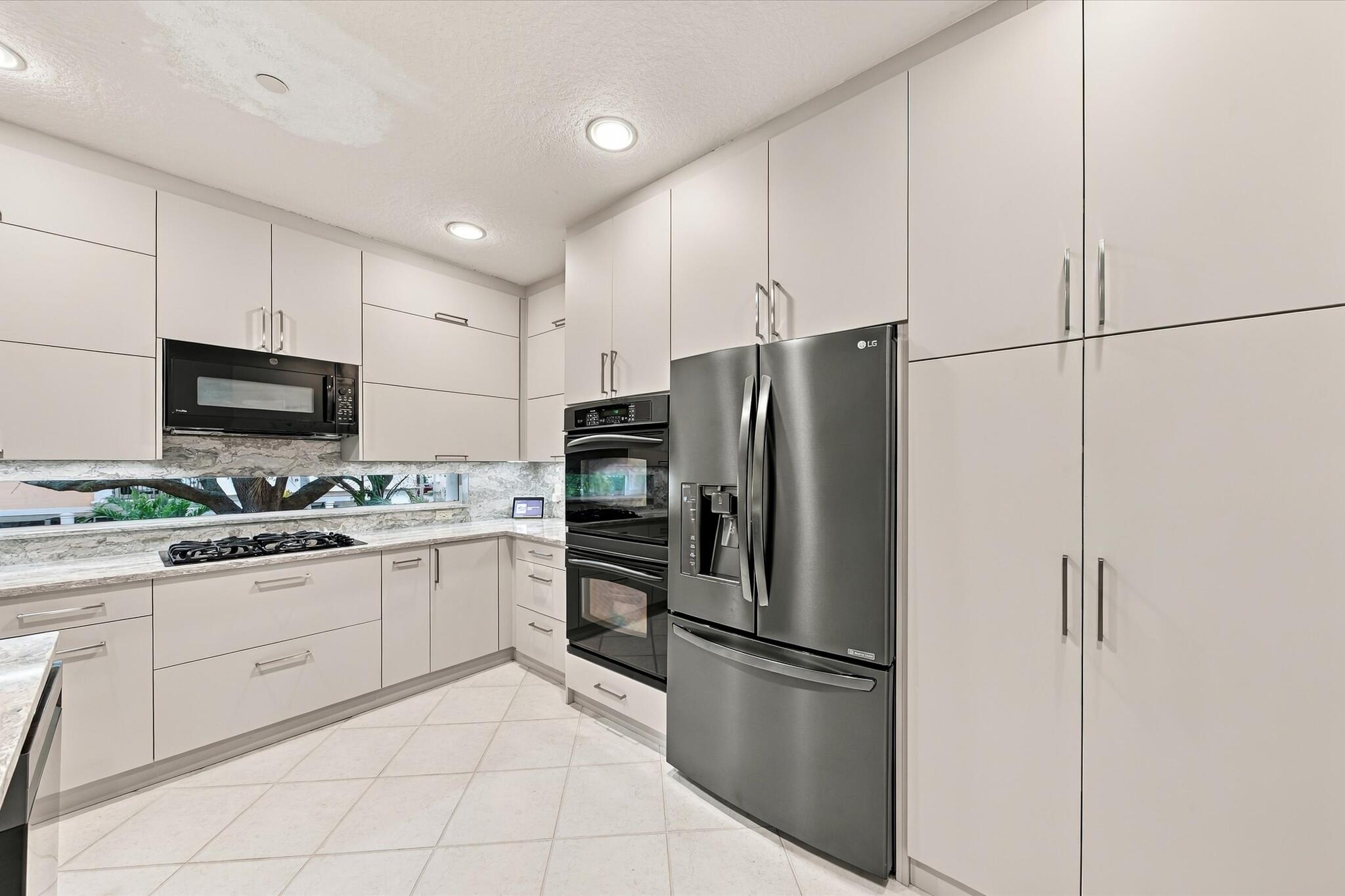 Kitchen featuring flat-panel cabinetry, stainless steel wall-mounted oven and microwave, stainless steel French-door refrigerator, integrated cooktop, and horizontal ribbon window backsplash
