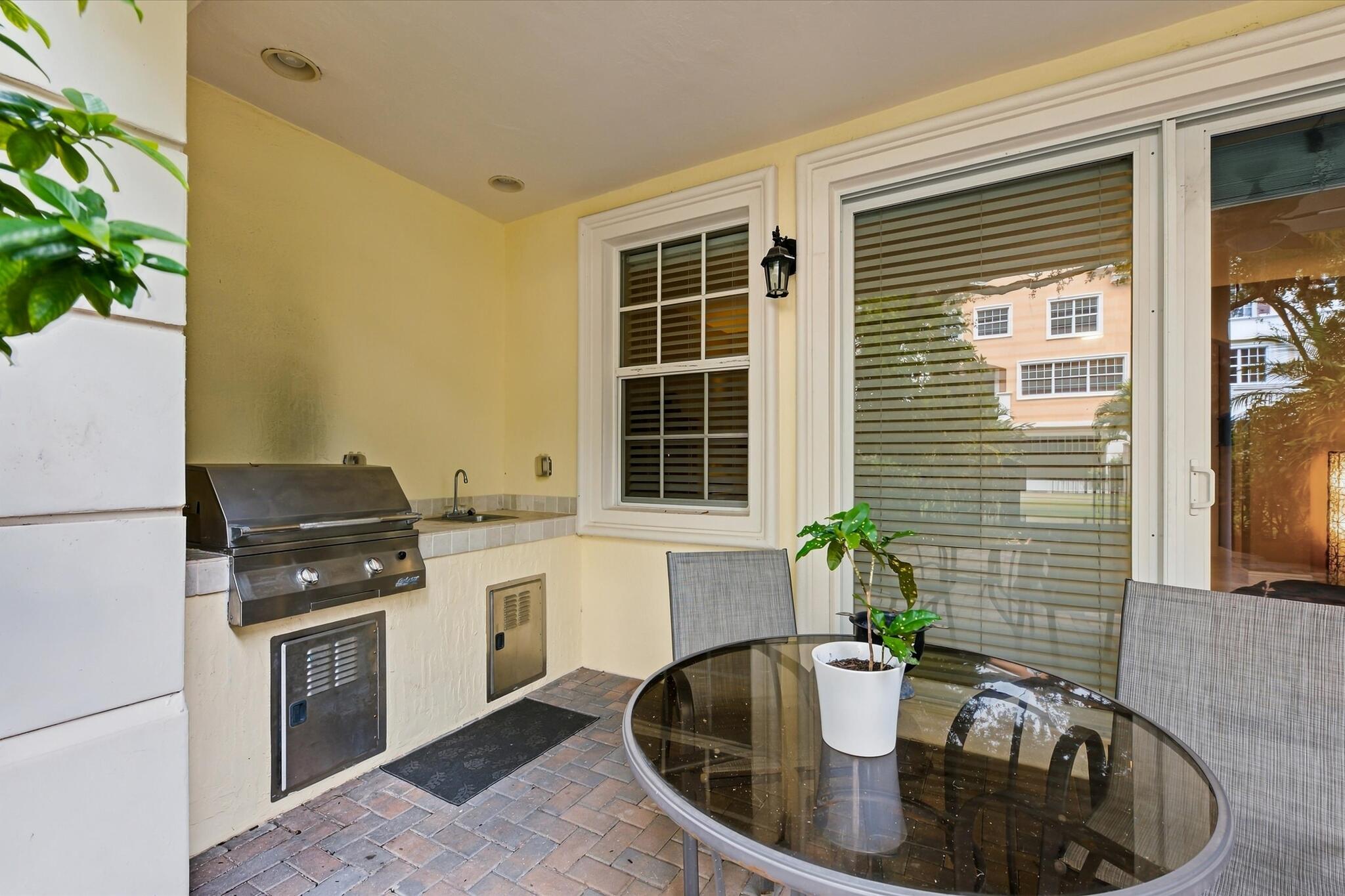 Covered outdoor kitchen featuring brick paver flooring, stainless steel built-in grill, stone-finish countertop, integrated sink, and recessed lighting