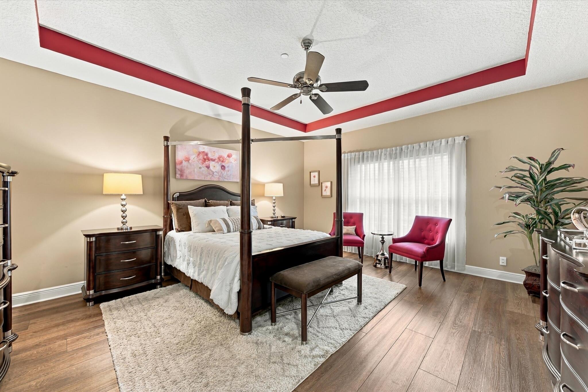 Tray ceiling with recessed architectural detail, wood-finish flooring, and a central ceiling fan with integrated lighting