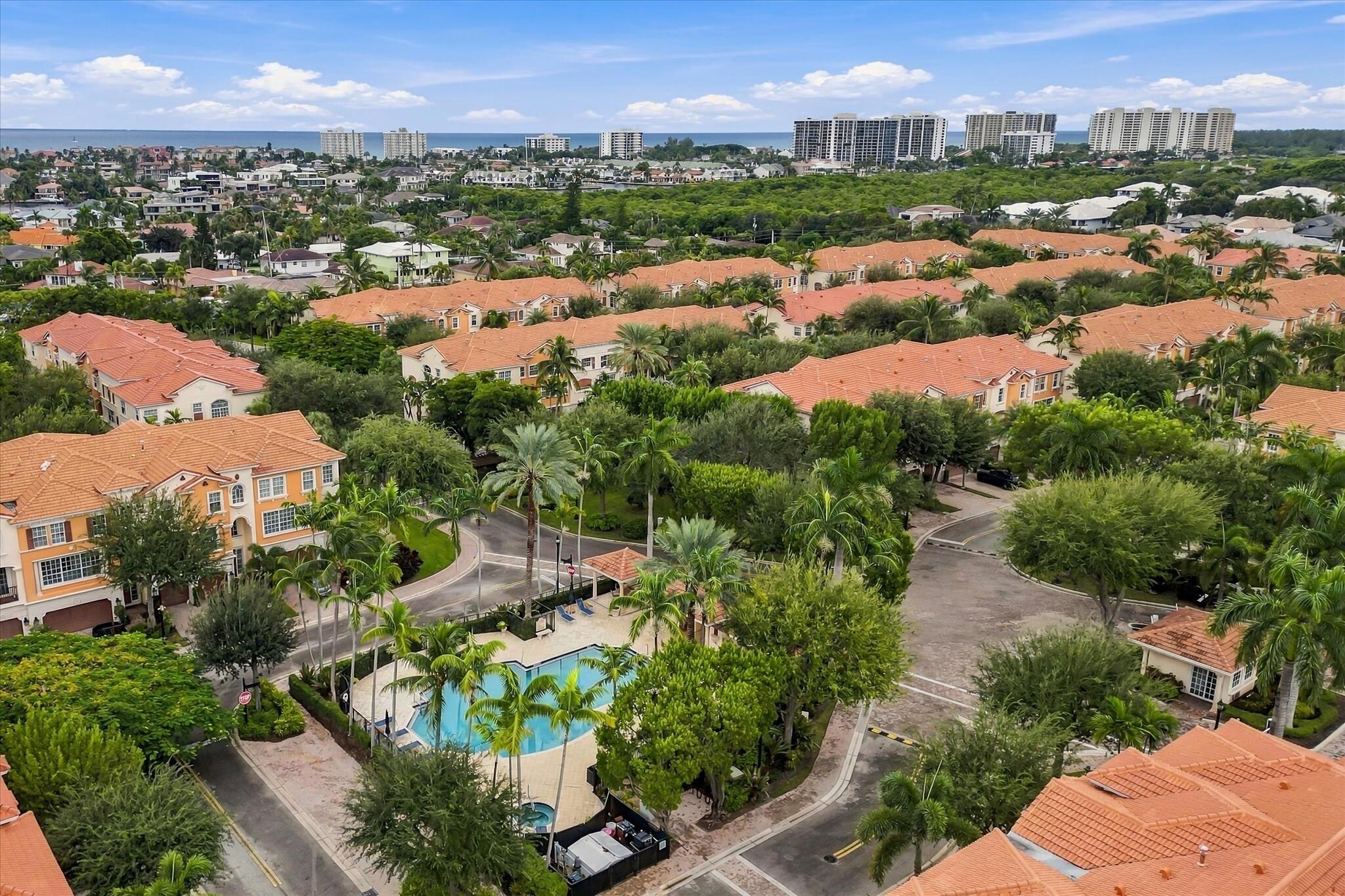 Aerial perspective featuring tile-roofed architecture, palm-lined landscaping, a communal swimming pool, and a coastal horizon