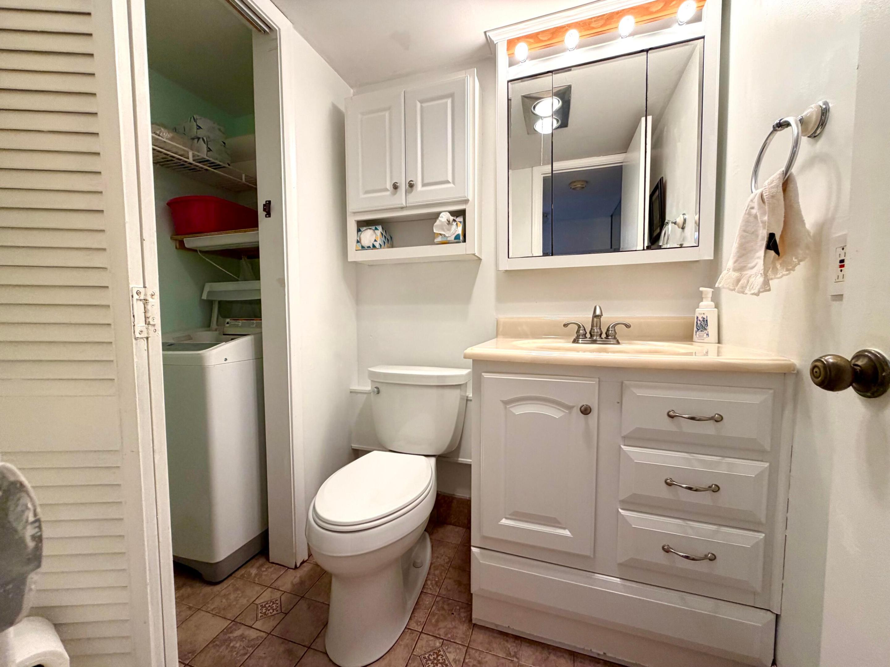 Bathroom featuring a white vanity with multi-drawer storage, integrated mirrored medicine cabinet with overhead lighting, tile flooring, and a dedicated laundry area with built-in shelving