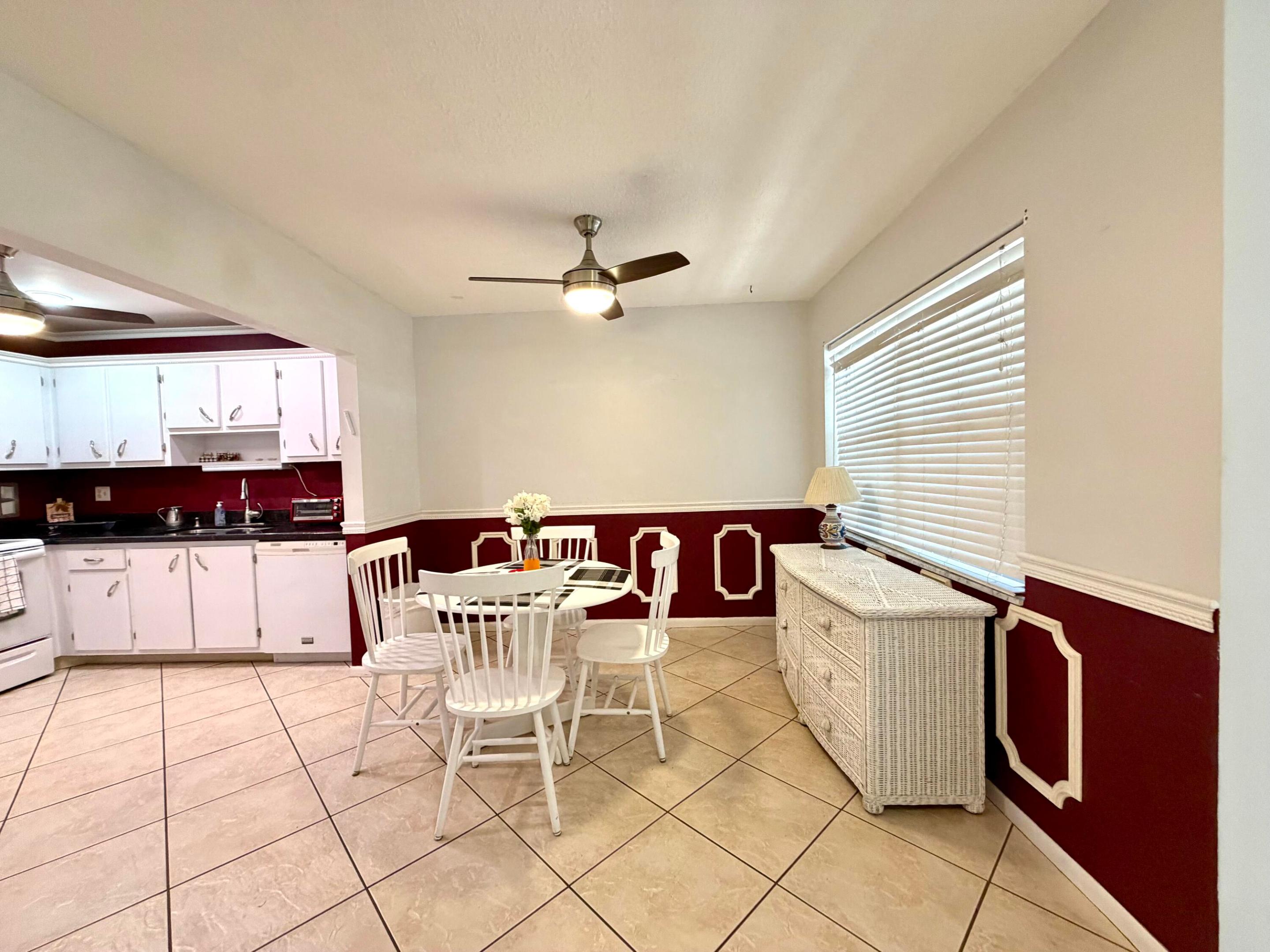 Dining area featuring diamond-pattern tile flooring, dual-tone wall paint with applied wainscoting, and a central ceiling fan with integrated lighting