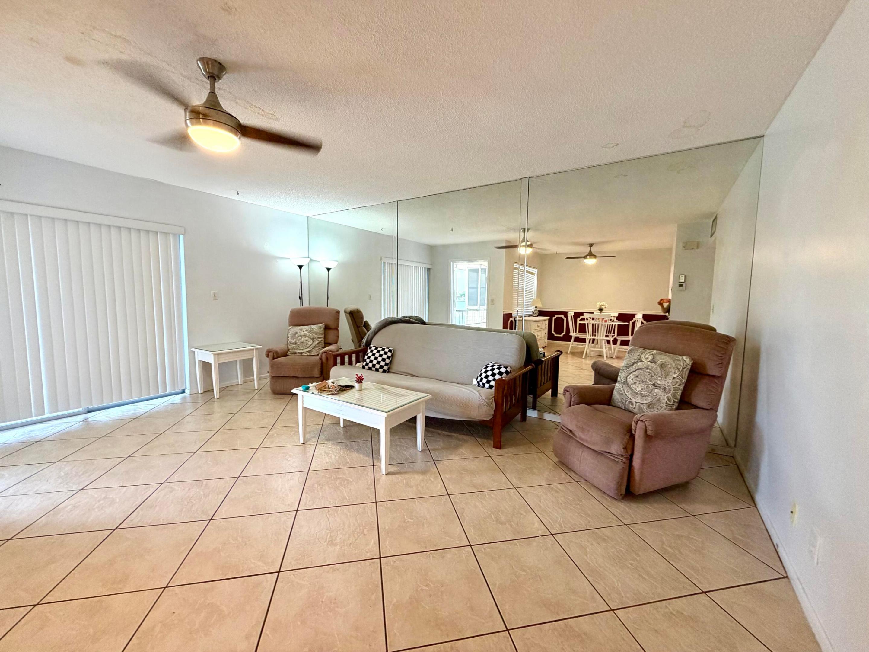 Neutral-toned ceramic tile flooring, floor-to-ceiling mirrored wall, and overhead ceiling fan with integrated lighting