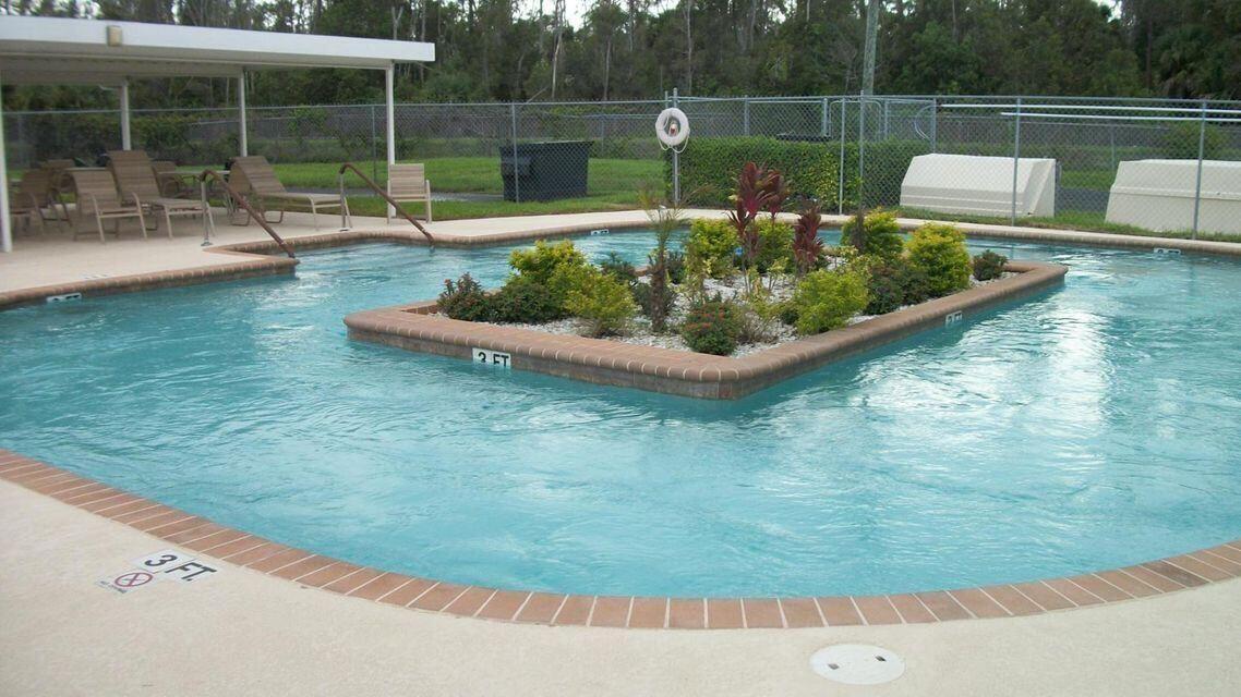 Swimming pool featuring a central planter island with shrubbery, brick coping, and a covered poolside patio area