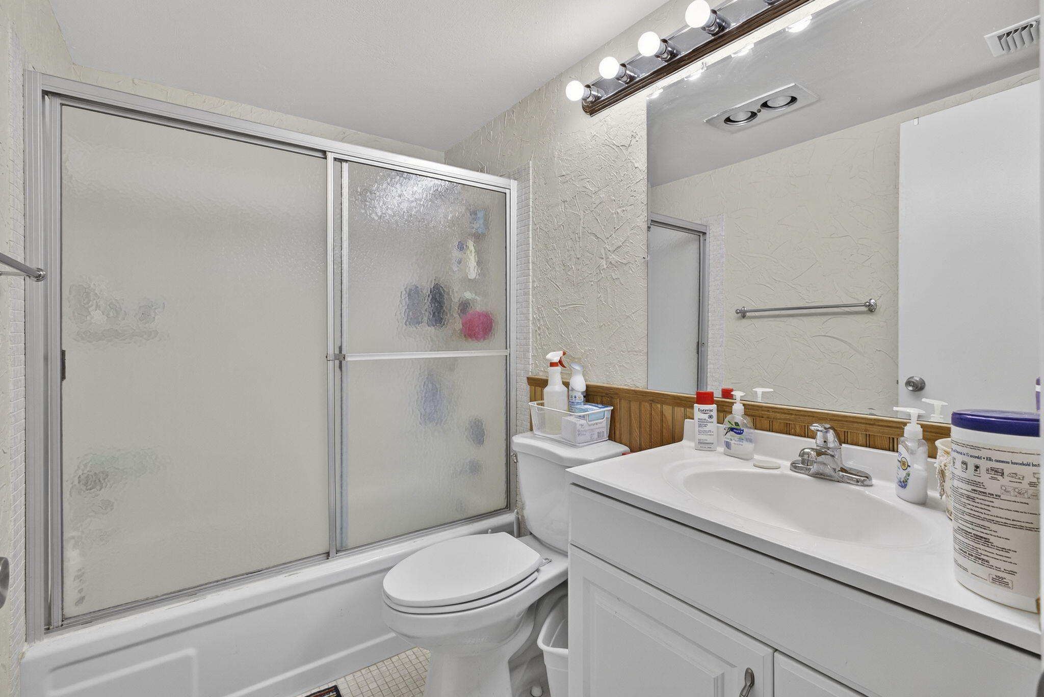 Bathroom featuring a white vanity cabinet with an integrated sink, polished metal faucet, full-width wall mirror, and a tub-shower combination with sliding glass doors