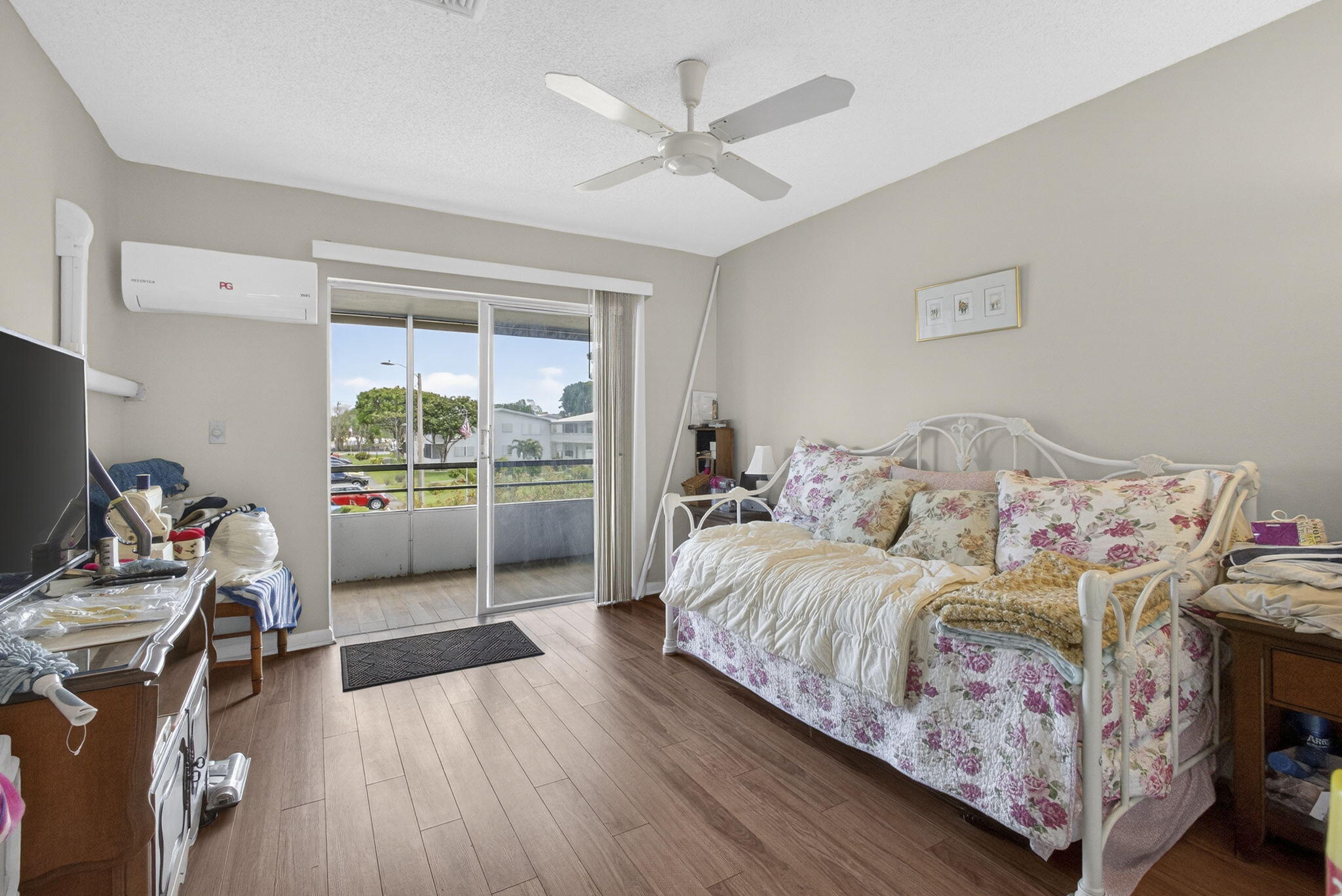 Room featuring wood-finish flooring, a wall-mounted ductless air conditioning unit, a ceiling fan, and sliding glass doors providing access to a balcony