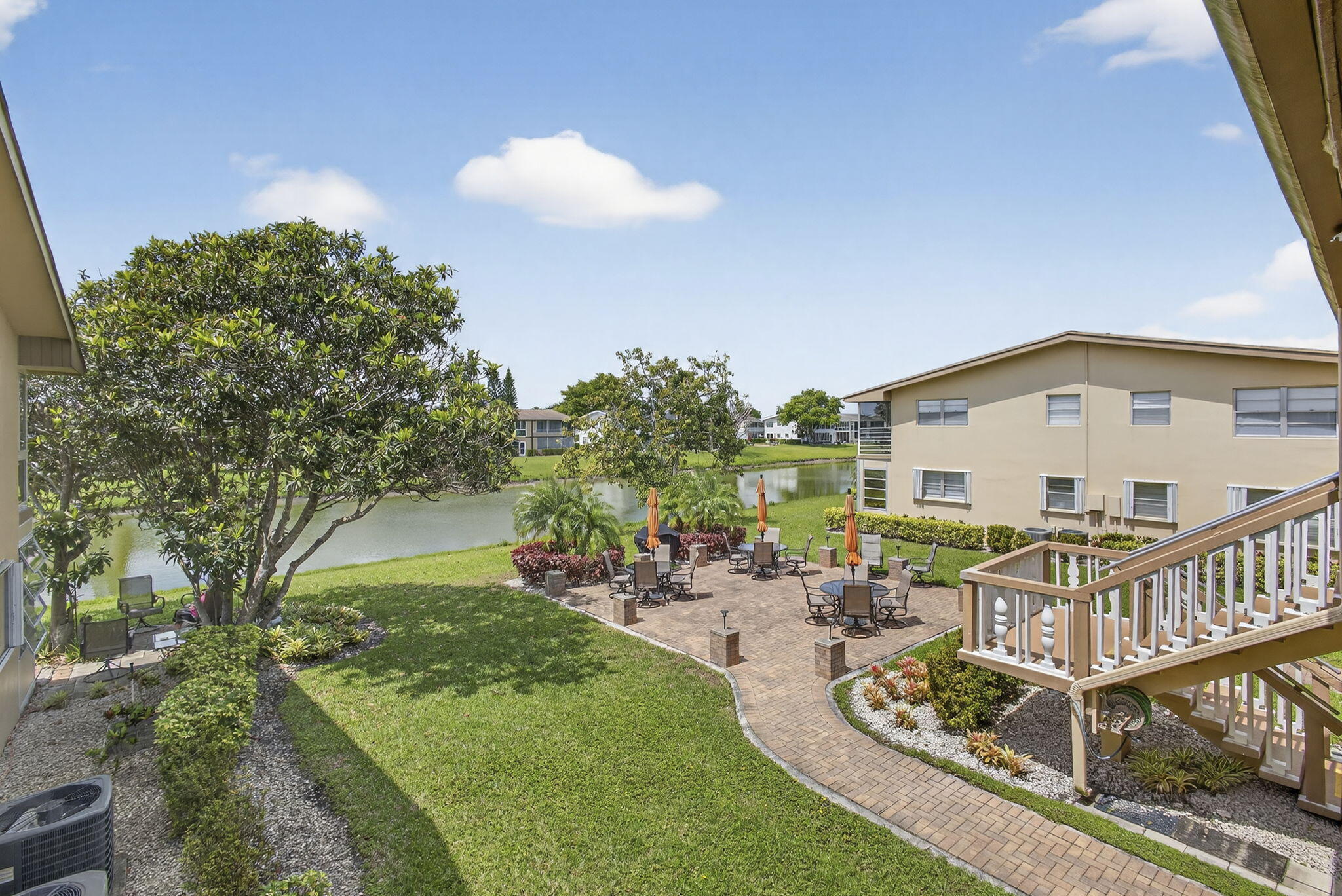 Paver patio, elevated wood deck with white balusters, waterfront property, and mature landscaping