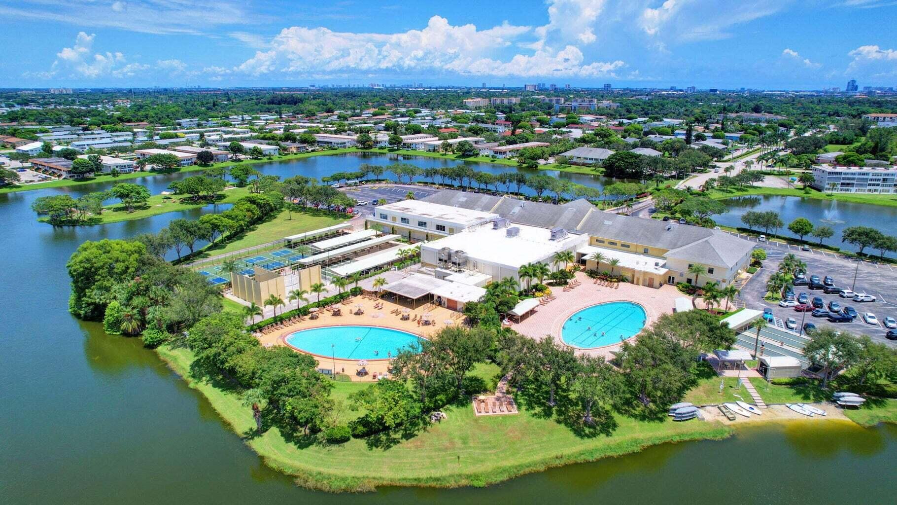Waterfront community grounds featuring two swimming pools, tennis courts, paved parking areas, and mature landscaping