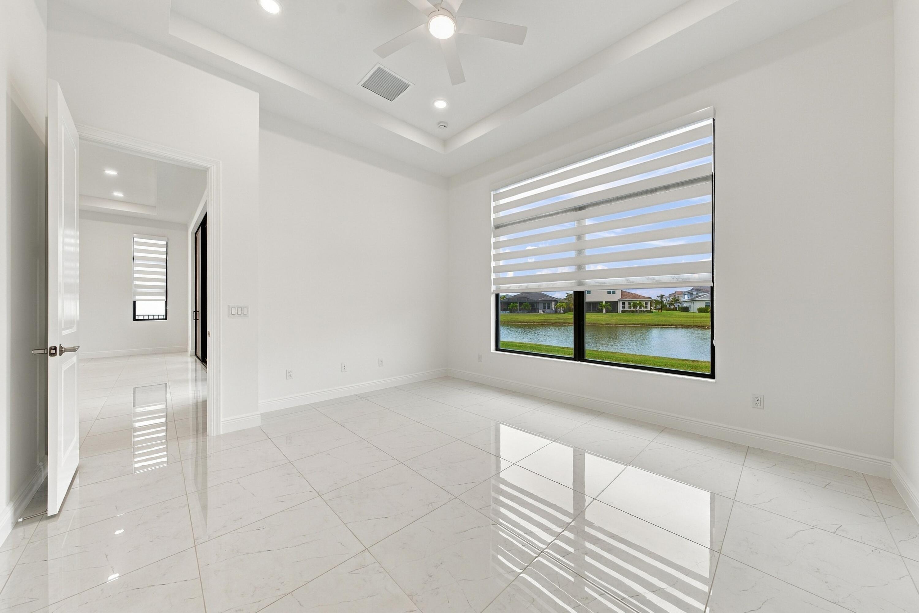 Primary suite with tray ceiling, ceiling fan and zebra blinds with lakefront views