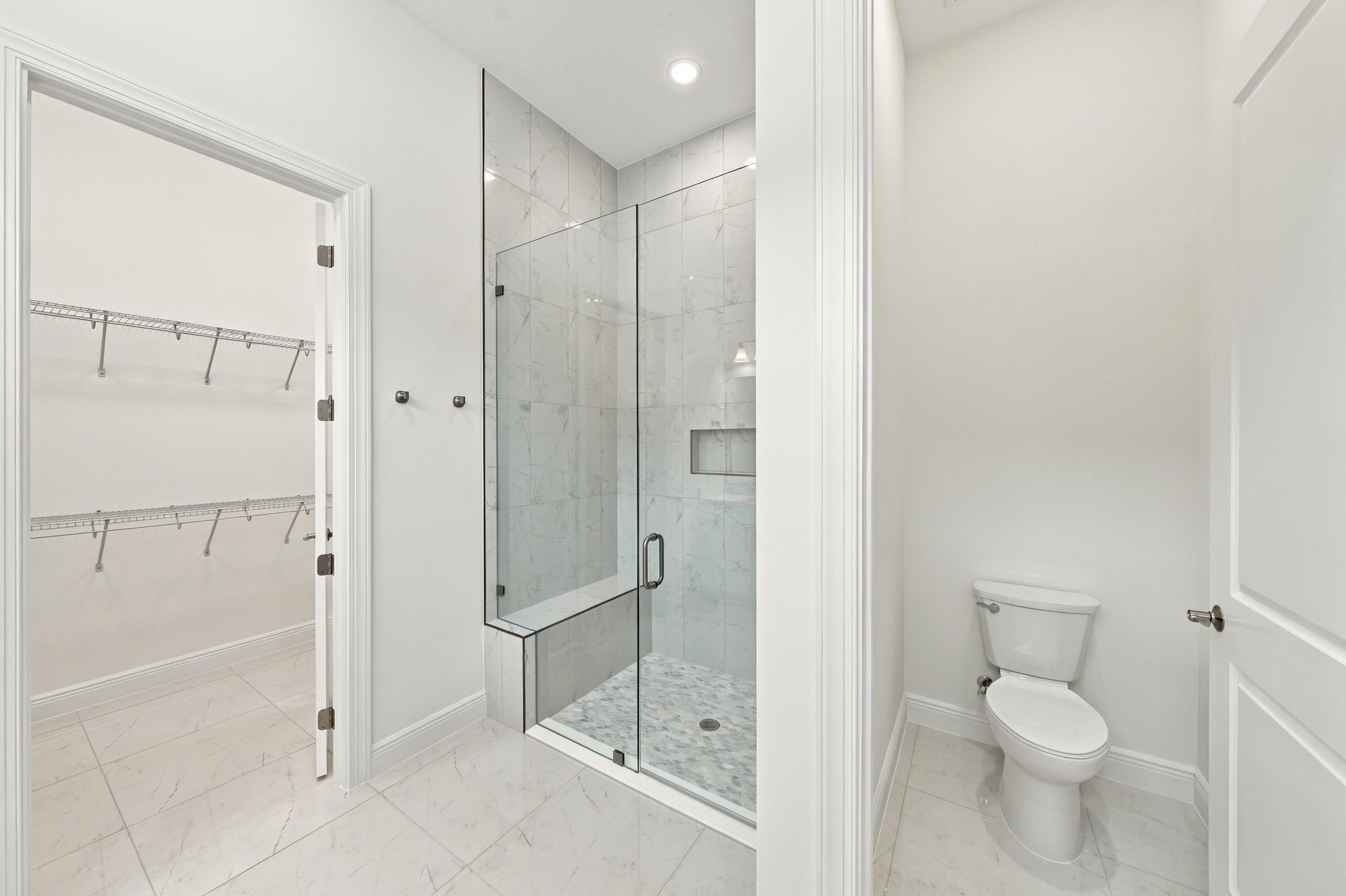 Primary bathroom frameless 96 inch glass shower with bench and upgraded tile to the ceiling with soft pebble shower floor, walk-in closet