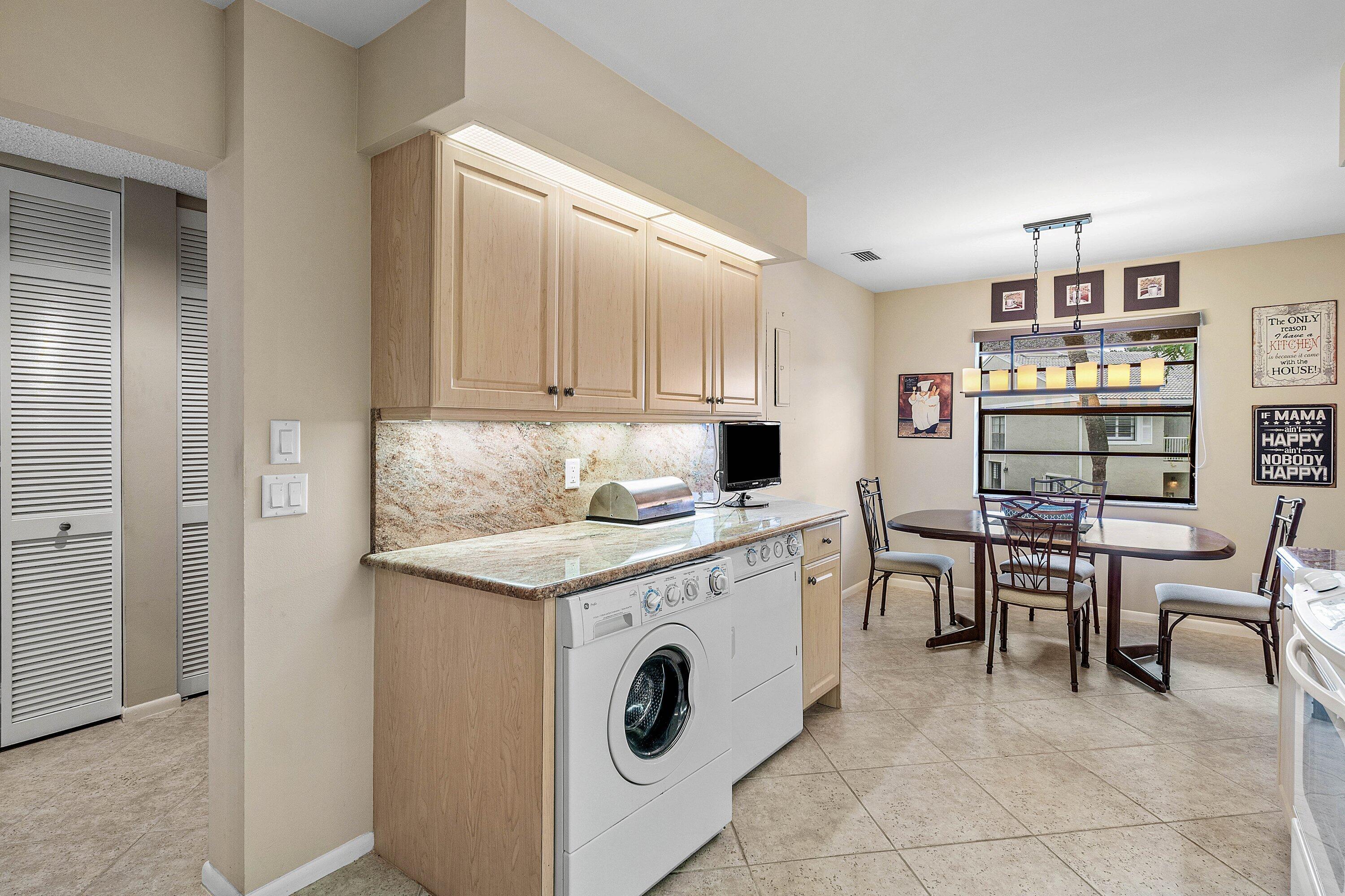 Utility area featuring light-finish cabinetry, stone-surface countertops, stone-tile backsplash, and integrated laundry appliances, complemented by stone-finish tile flooring