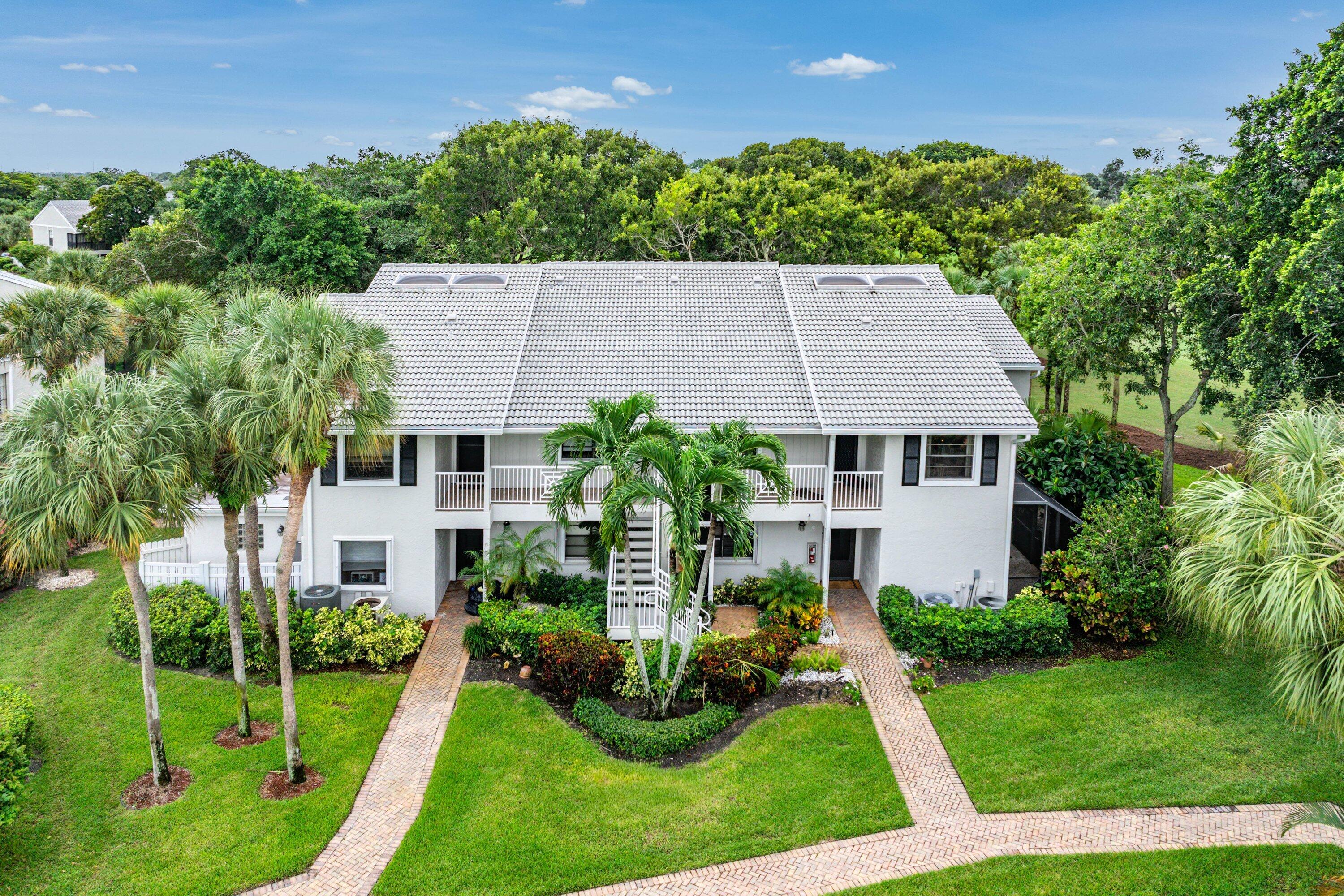 Multi-story residence featuring a tile roof, brick paver walkways, mature palm trees, manicured landscaping, and second-level balcony railings