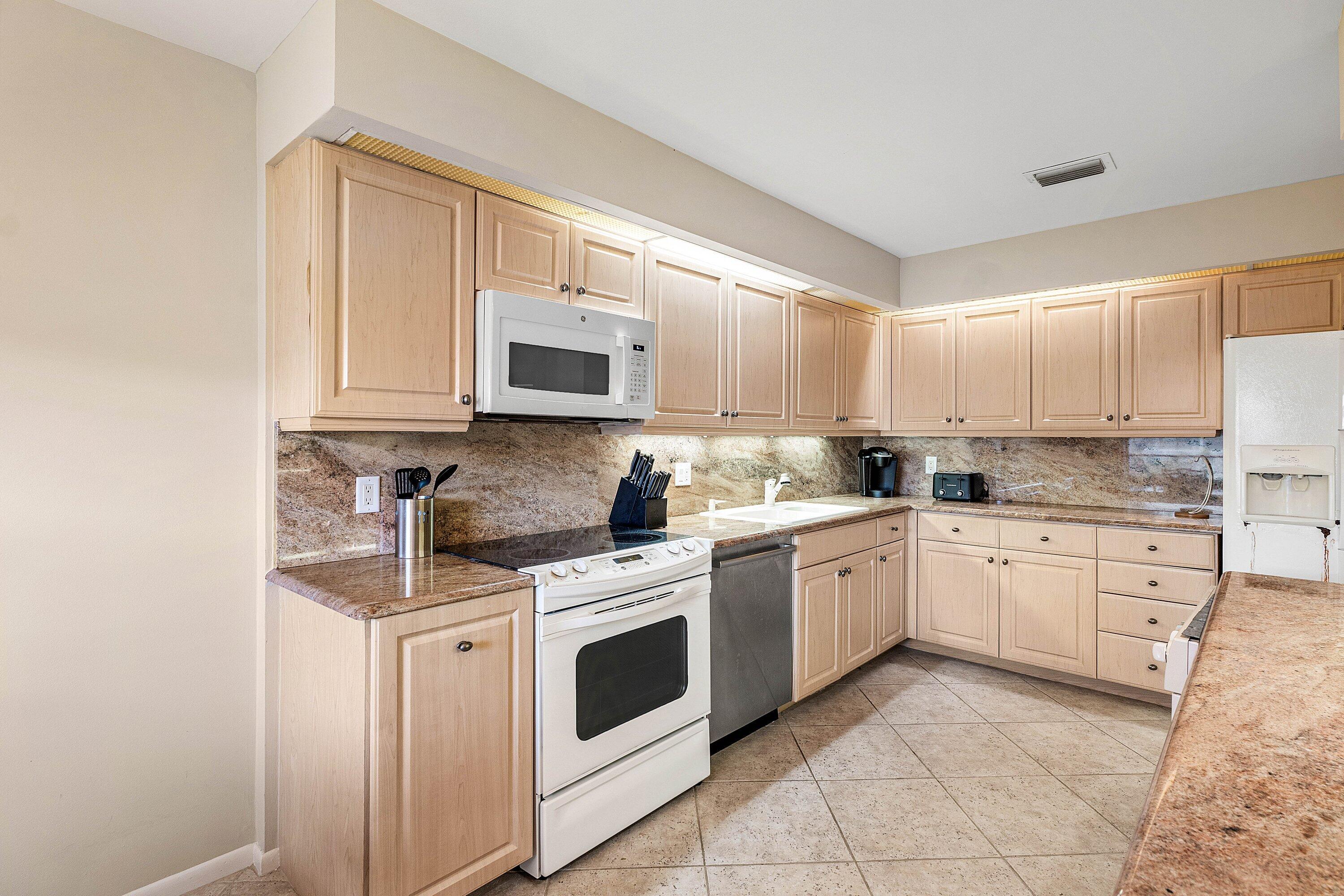 Kitchen featuring light wood cabinetry, stone countertops, integrated under-cabinet lighting, tile flooring, and stainless steel dishwasher