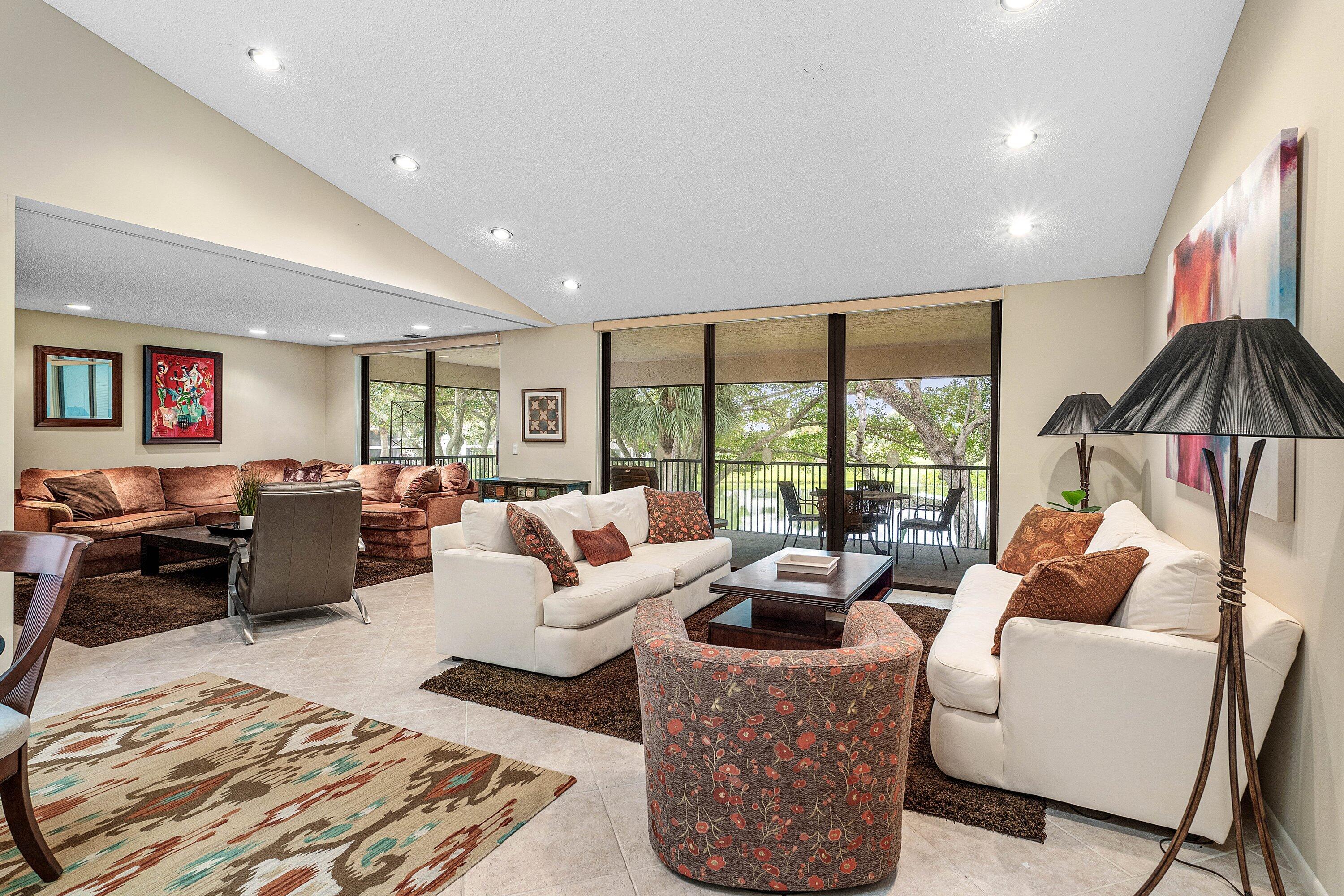 Vaulted ceilings with recessed lighting, large-format tile flooring, and floor-to-ceiling glass sliding doors opening to a covered balcony