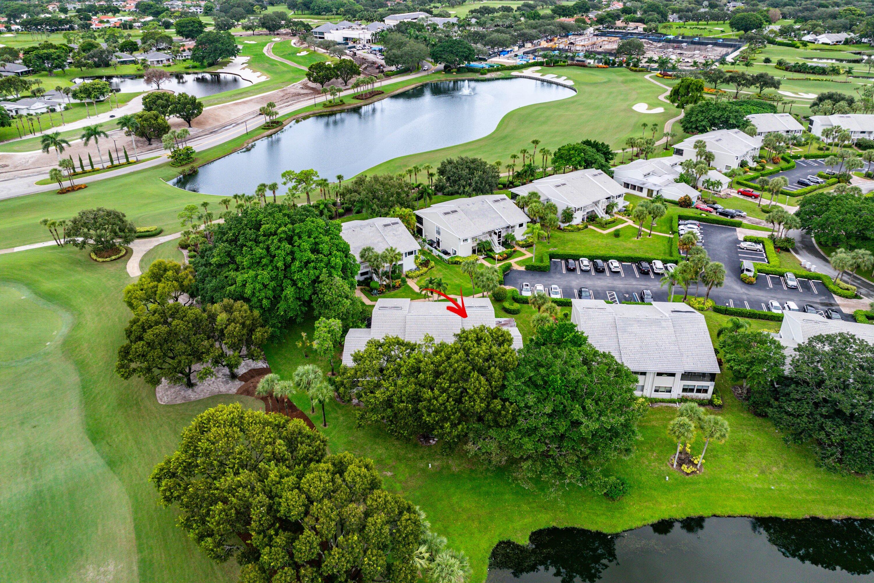 Aerial perspective of a multi-unit residential building featuring a tile roof, established landscaping, and proximity to a golf course and a lake