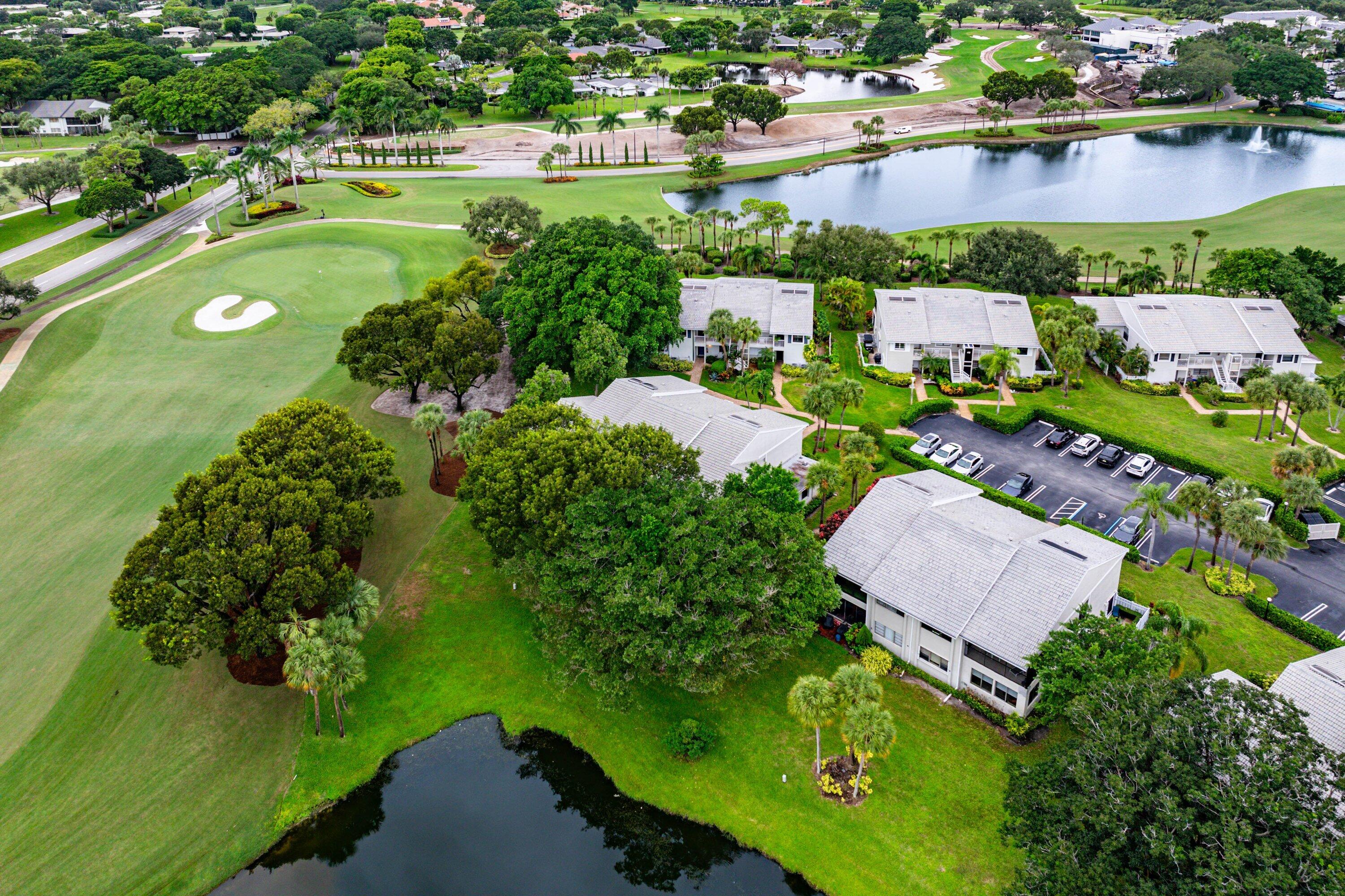 Aerial perspective featuring multi-story residential structures, manicured lawn areas, mature tree canopy, and direct water frontage