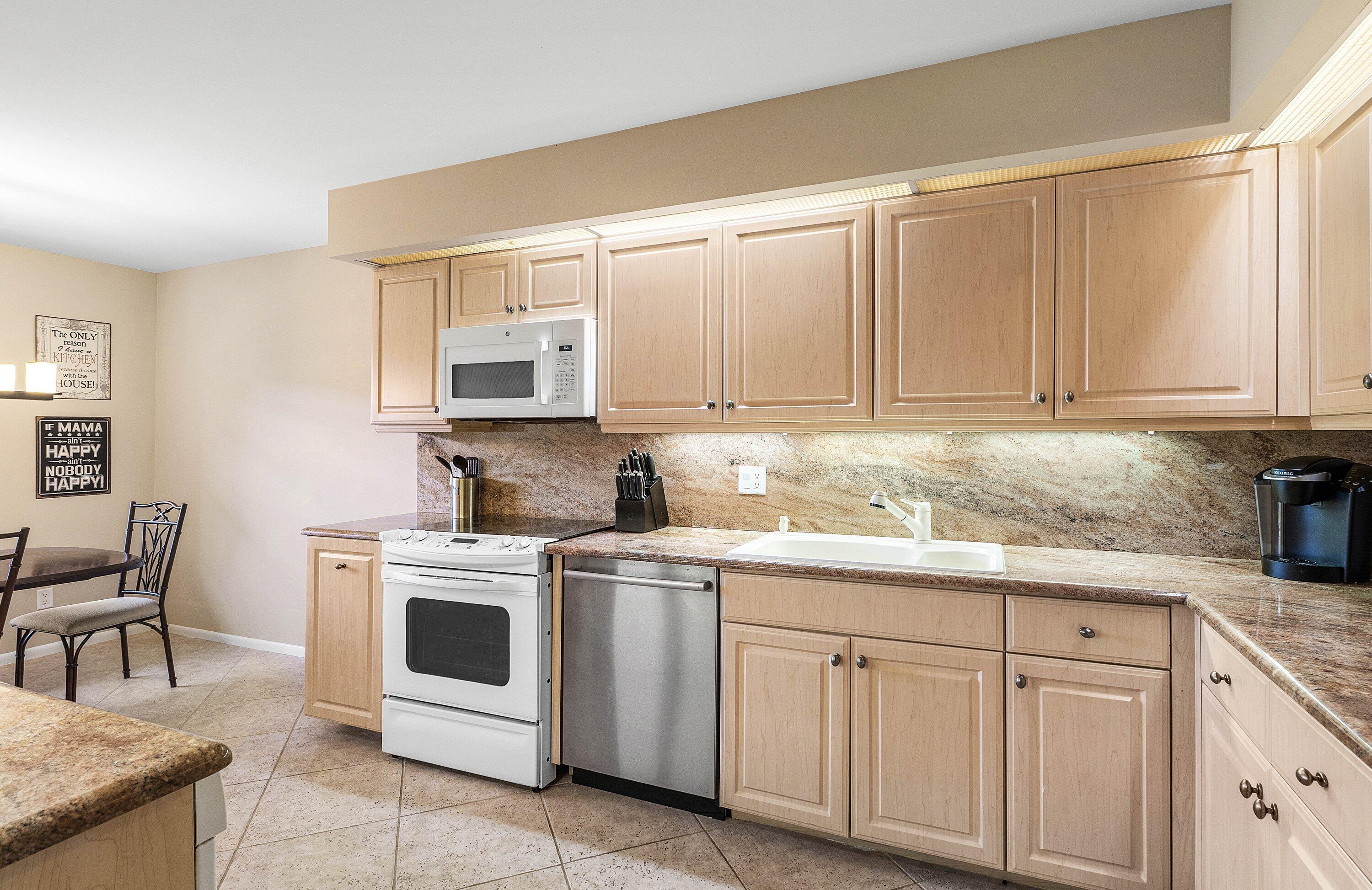 Kitchen featuring light wood cabinetry, stone-finish countertops, tile flooring, integrated under-cabinet lighting, and a stainless steel dishwasher