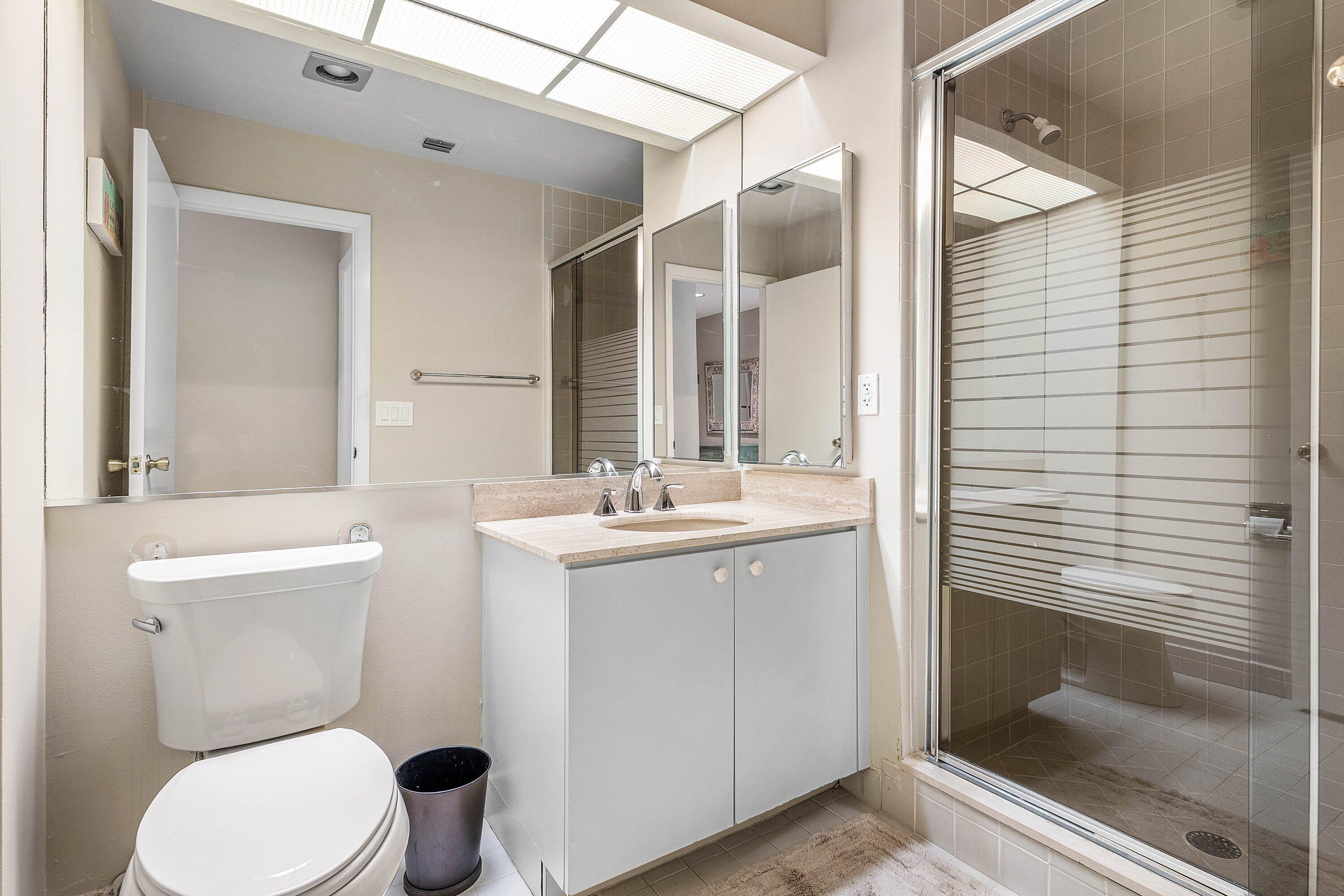 Bathroom featuring a single-sink vanity with light-toned countertop, floor-to-ceiling mirror, integrated recessed lighting, and a glass-enclosed shower with horizontal-patterned frosted privacy glass
