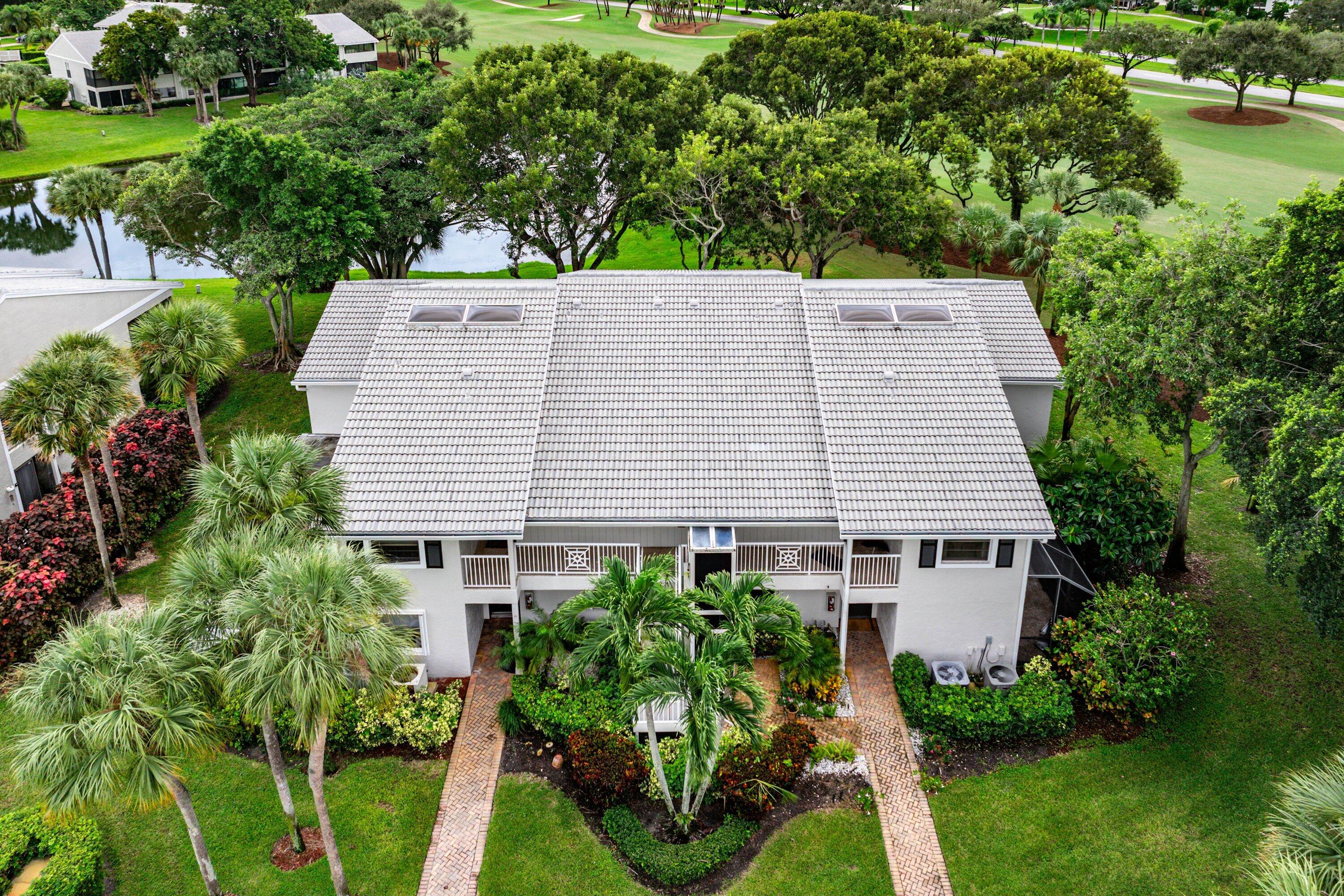 Two-story multi-unit structure featuring a tile roof, dual balconies, brick-paver walkways, and exterior landscaping, positioned on a golf course with water features