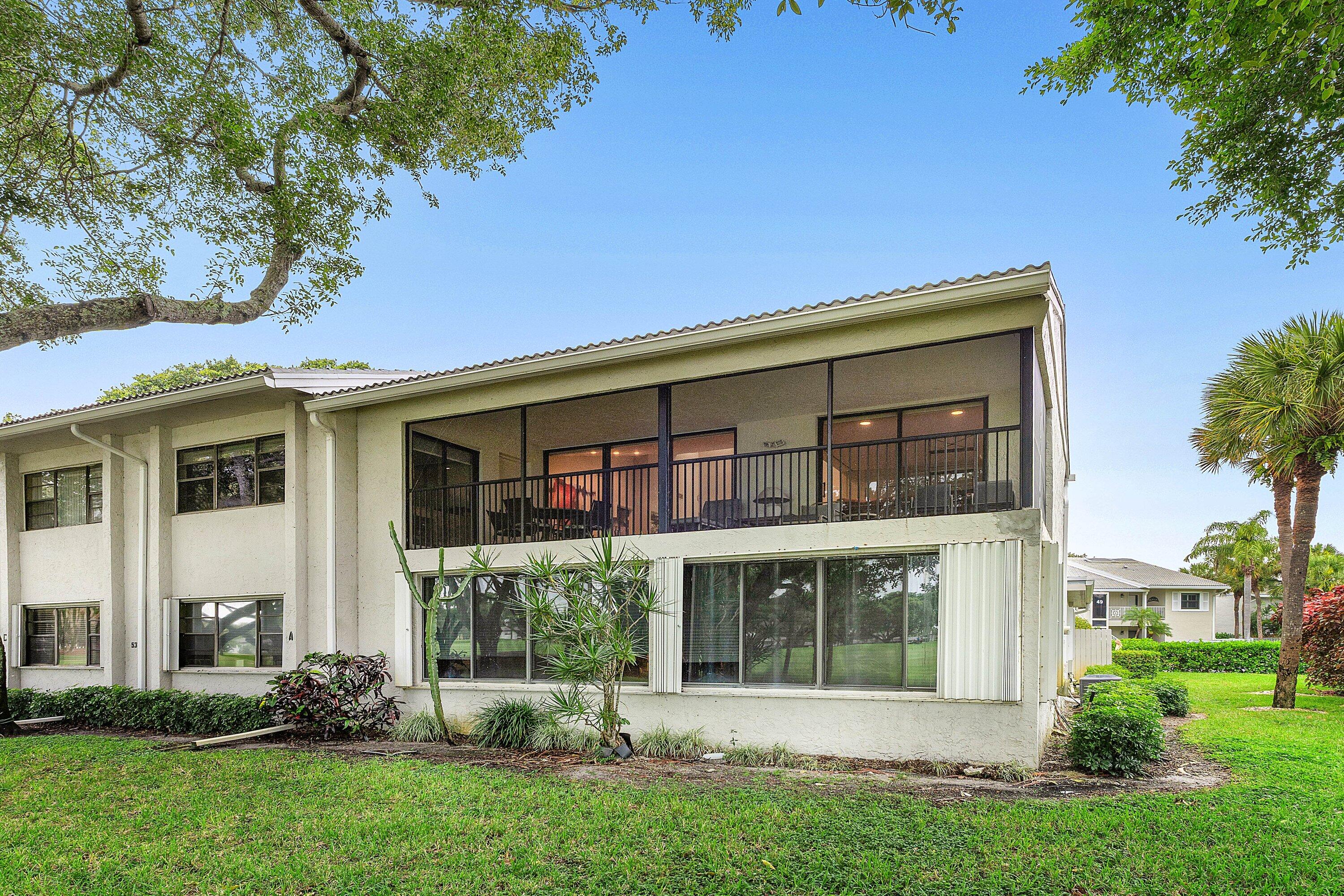 Two-story exterior featuring a screened-in second-level balcony with metal railing, floor-to-ceiling windows on the ground level, and mature landscaping