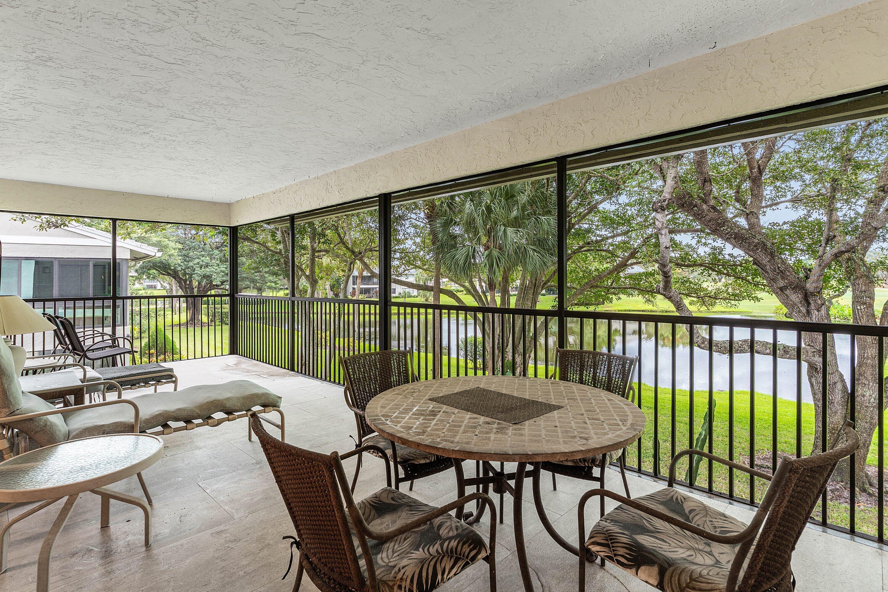 Screened-in lanai featuring tile flooring, a textured ceiling, and metal railings overlooking a water feature and mature trees