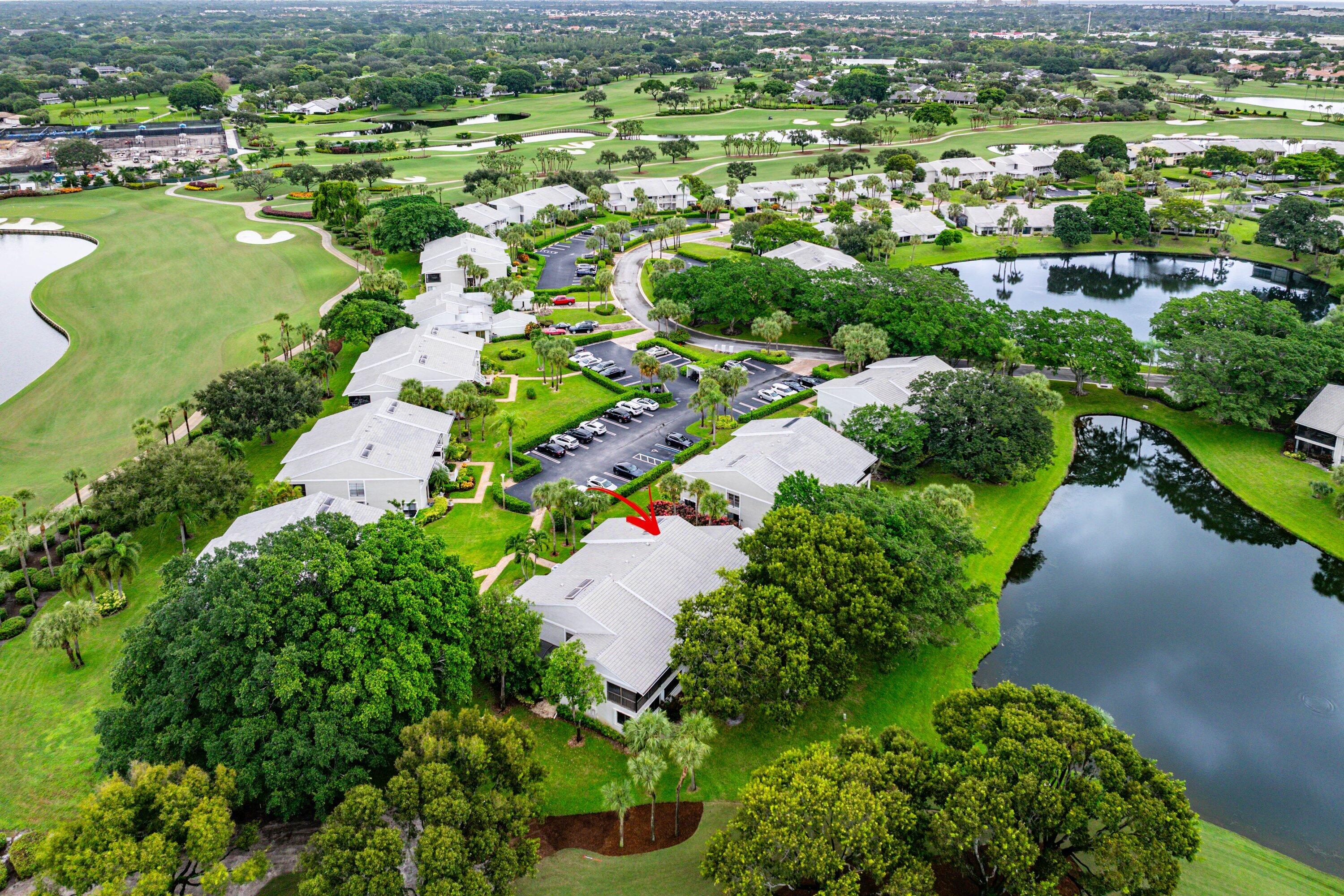 Aerial perspective of a multi-unit property featuring a shingle roof, paved surface parking, mature landscaping, and proximity to water elements and golf course grounds