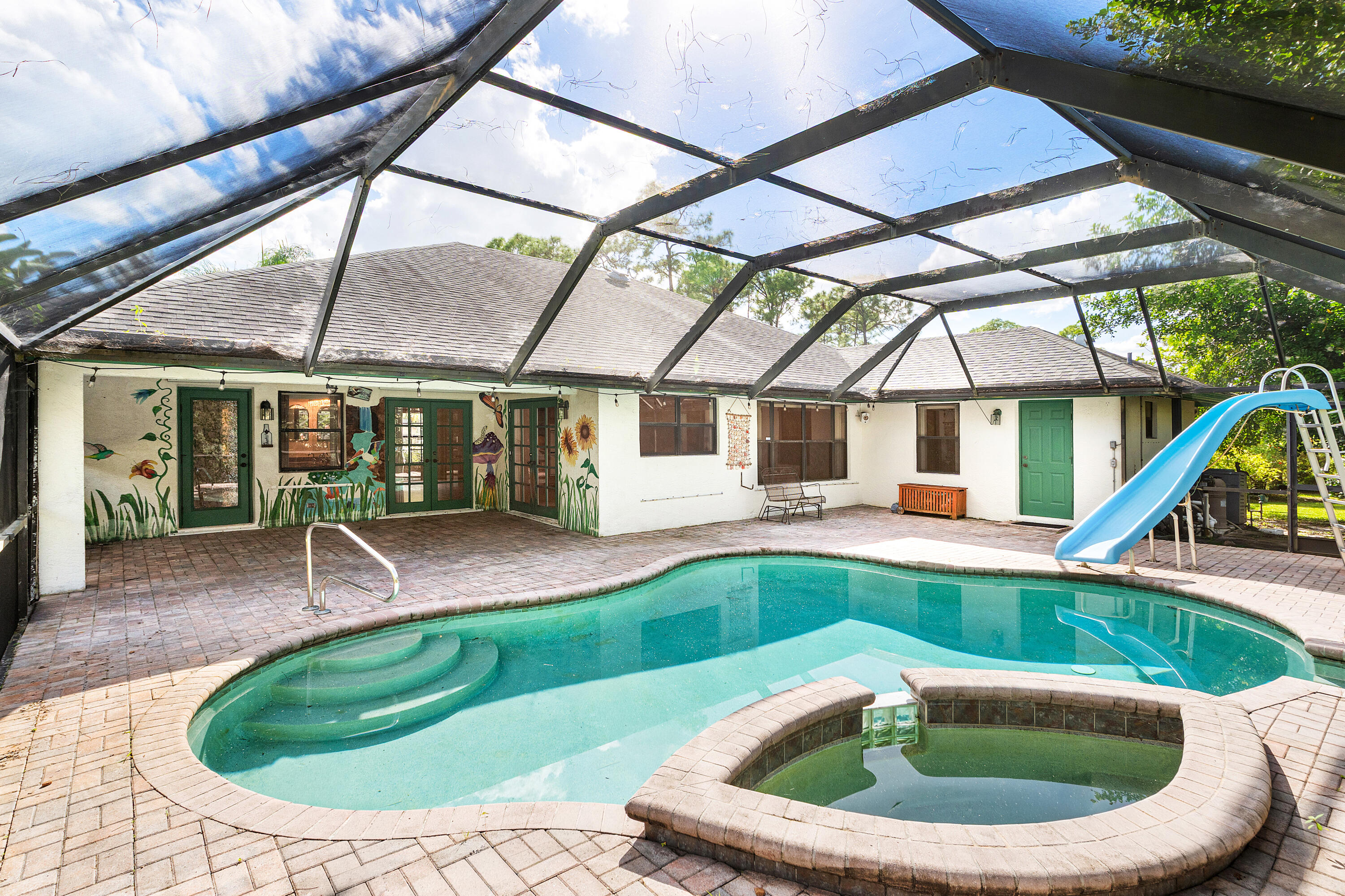 Screened-in patio featuring a brick-paver deck, an in-ground pool with integrated spillover spa, and a built-in water slide